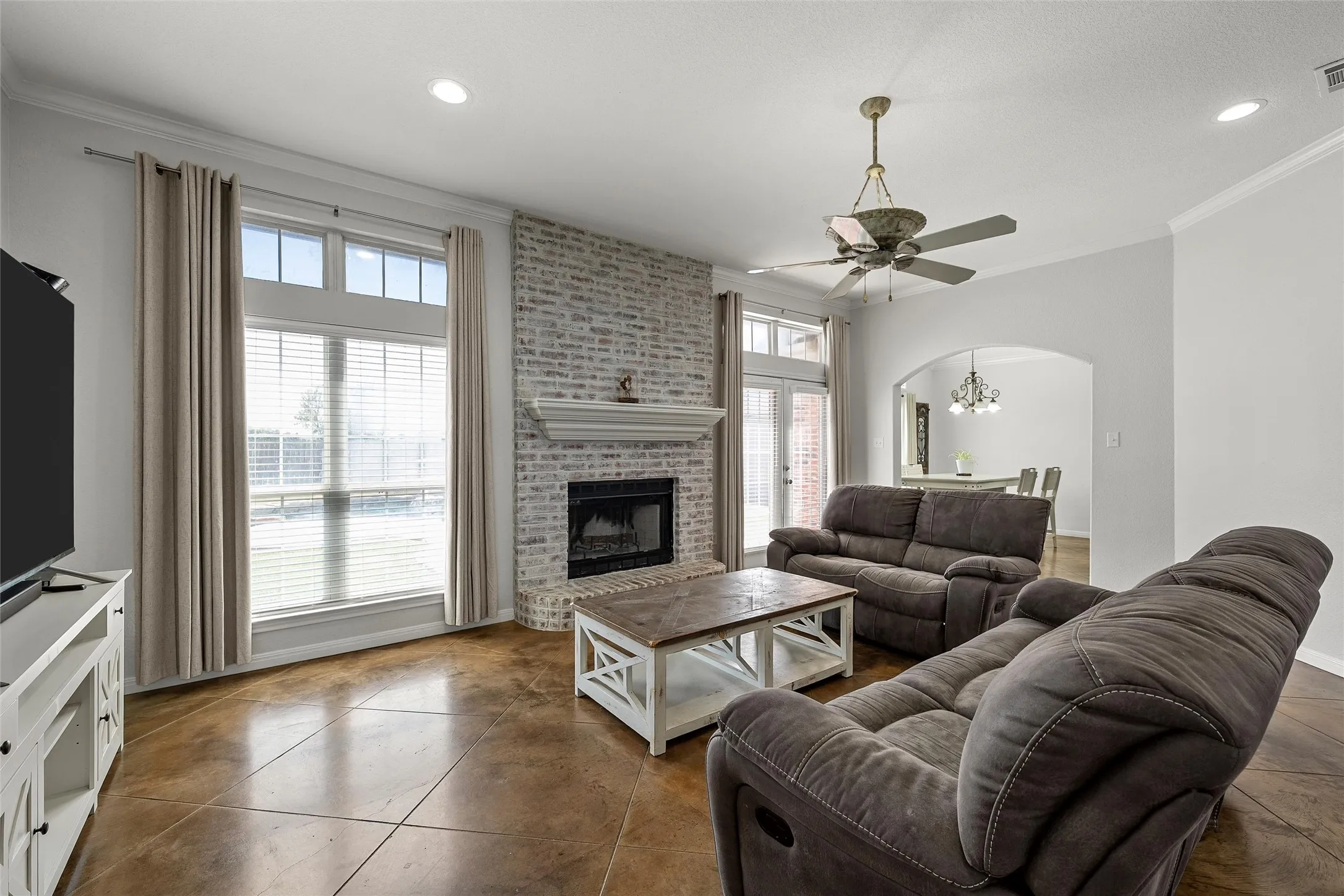 Living area featuring acid-stained concrete flooring, a white-washed brick fireplace with a mantle, and large windows with transom accents