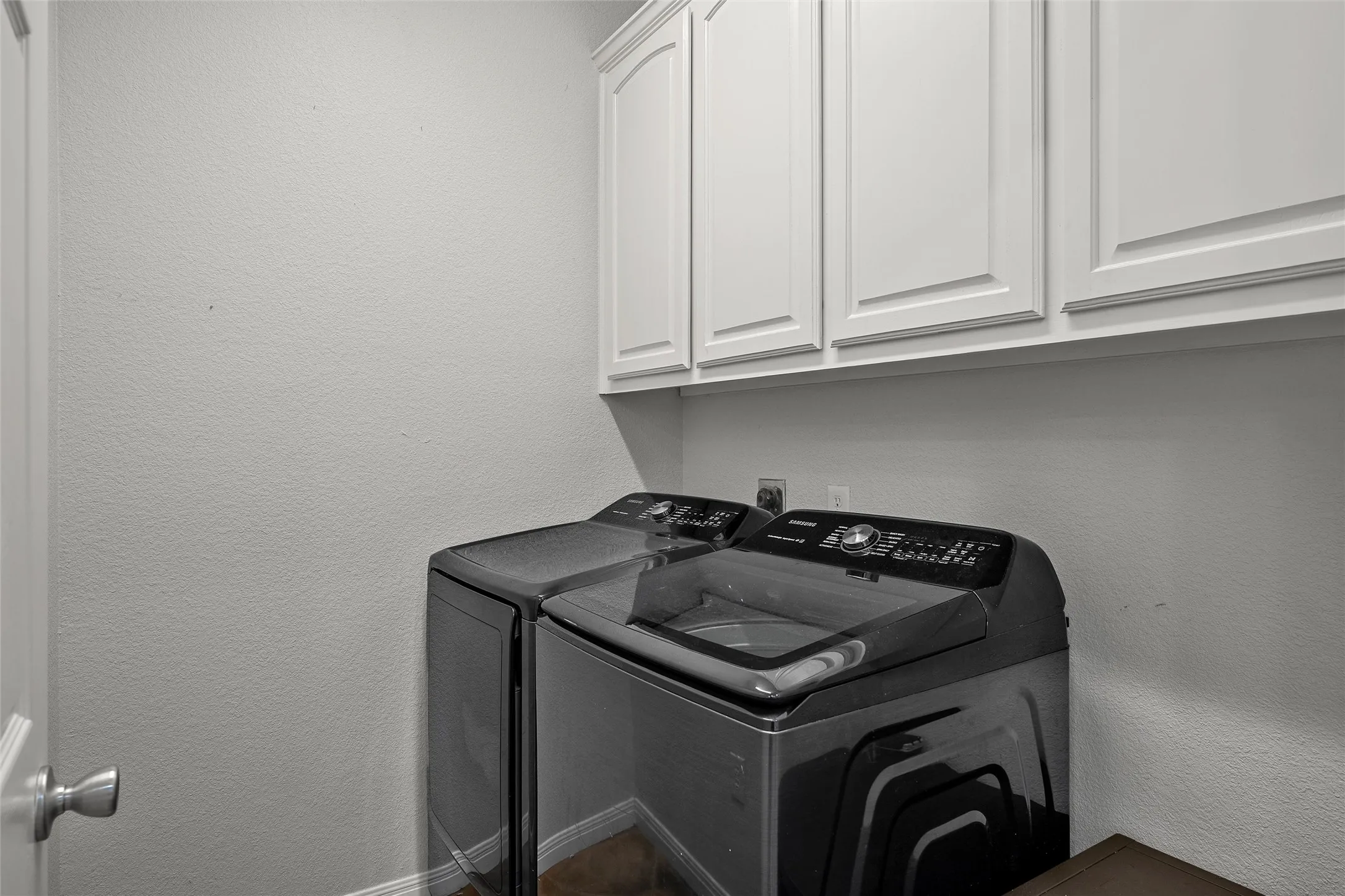 Dedicated laundry space featuring white upper cabinetry, wood-finish flooring, and light-toned walls