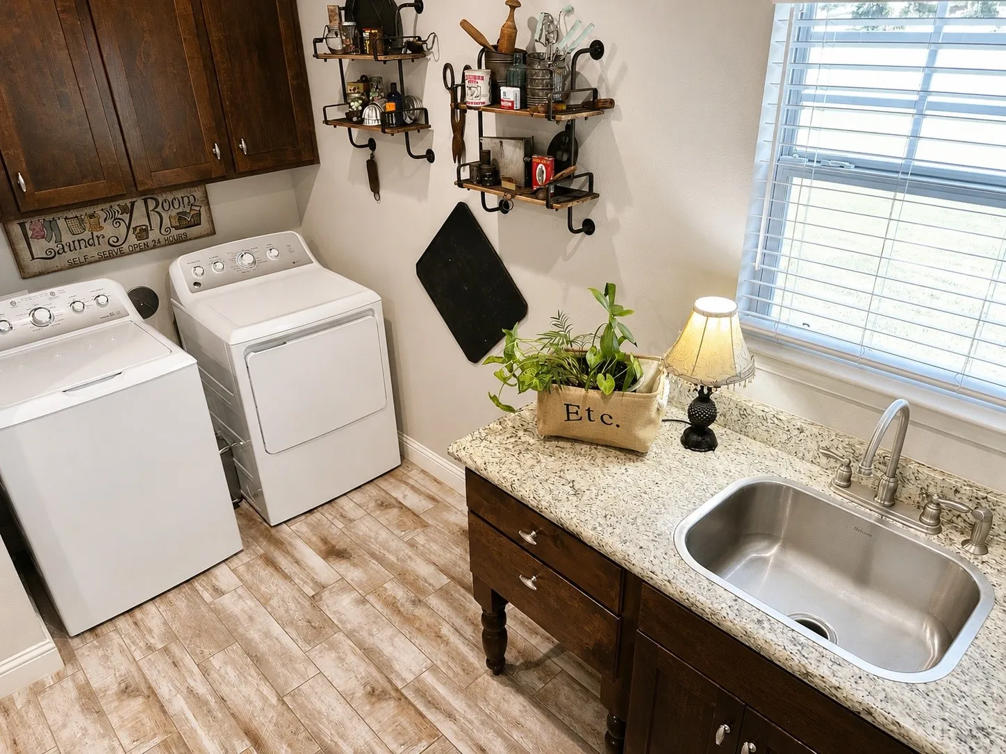Laundry room featuring wood-finish flooring, dark wood cabinetry, granite-style countertops, a stainless steel sink, and a window with blinds