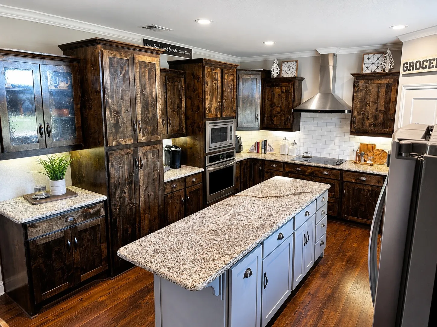 Kitchen featuring dark wood cabinetry, light granite countertops, a large center island with light blue base cabinetry, stainless steel appliances, and wood-finish flooring