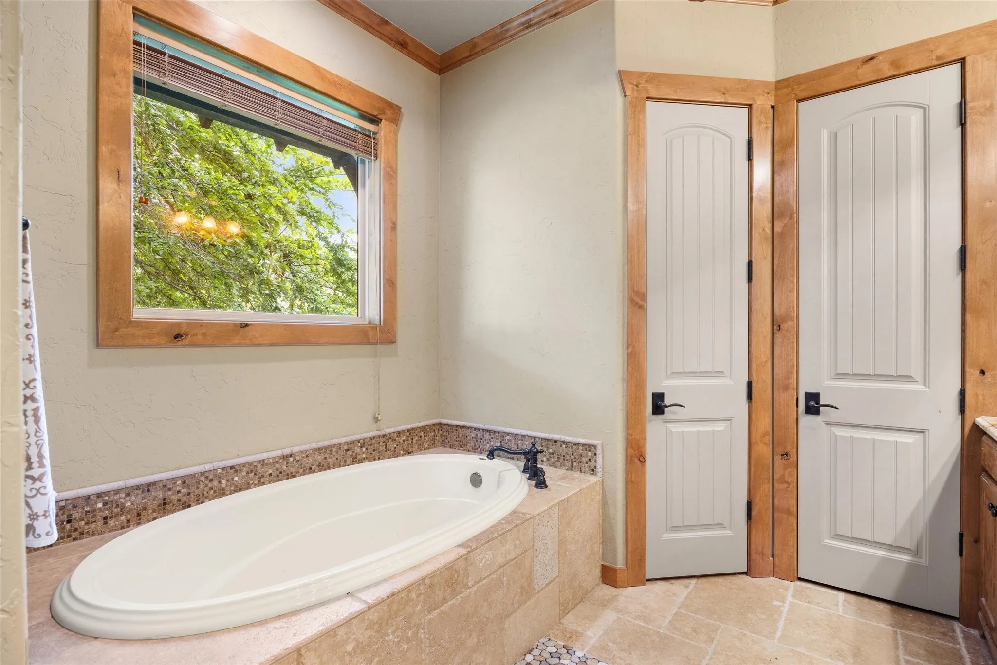 Soaking tub with a tiled surround, framed window, and two paneled doors with black hardware