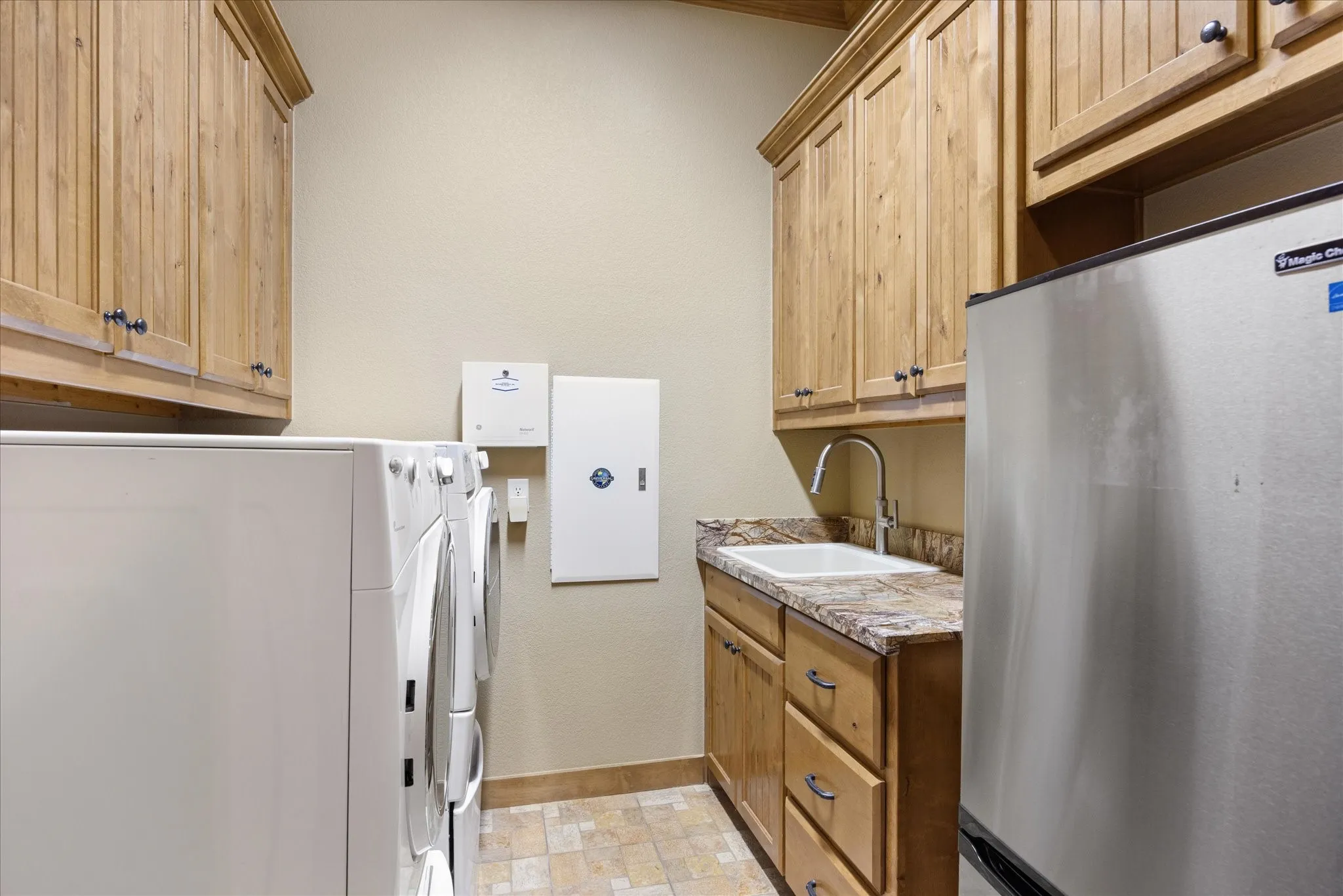 Functional laundry area featuring ample cabinetry, a built-in sink with a gooseneck faucet, a stone-finish countertop, and tile flooring