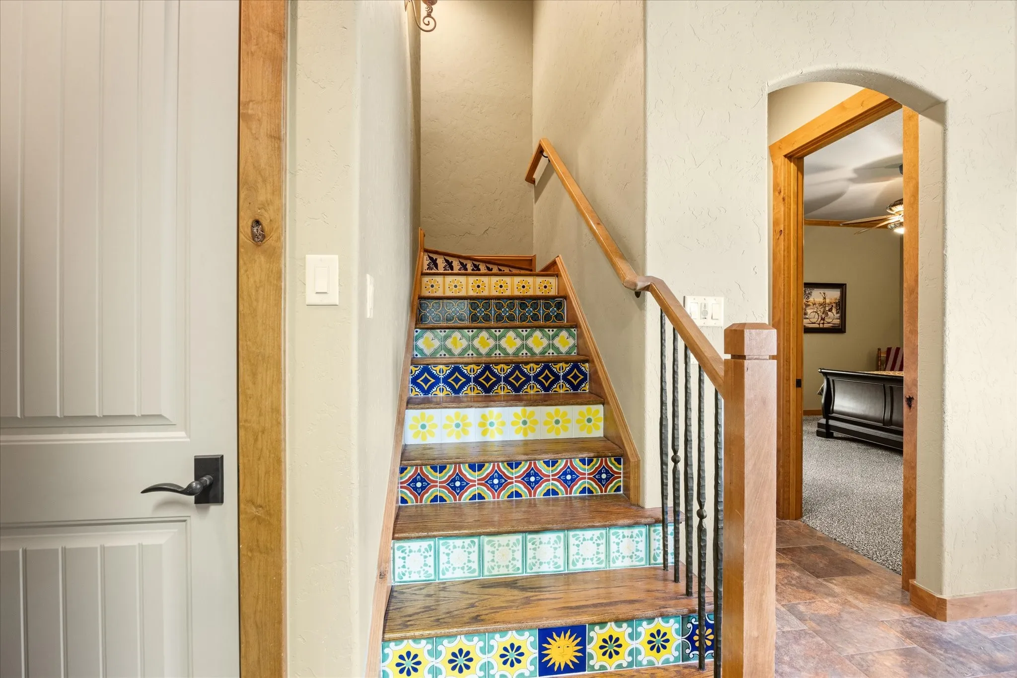 Staircase featuring decorative riser tiles, wood treads, and an iron baluster railing