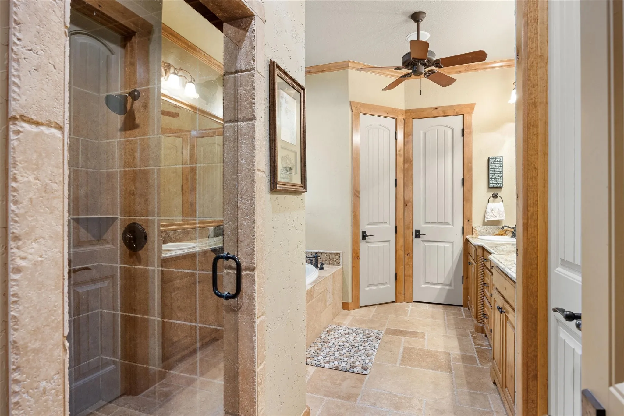 Expansive bathroom featuring natural stone tile flooring and a glass-enclosed shower with stone surround