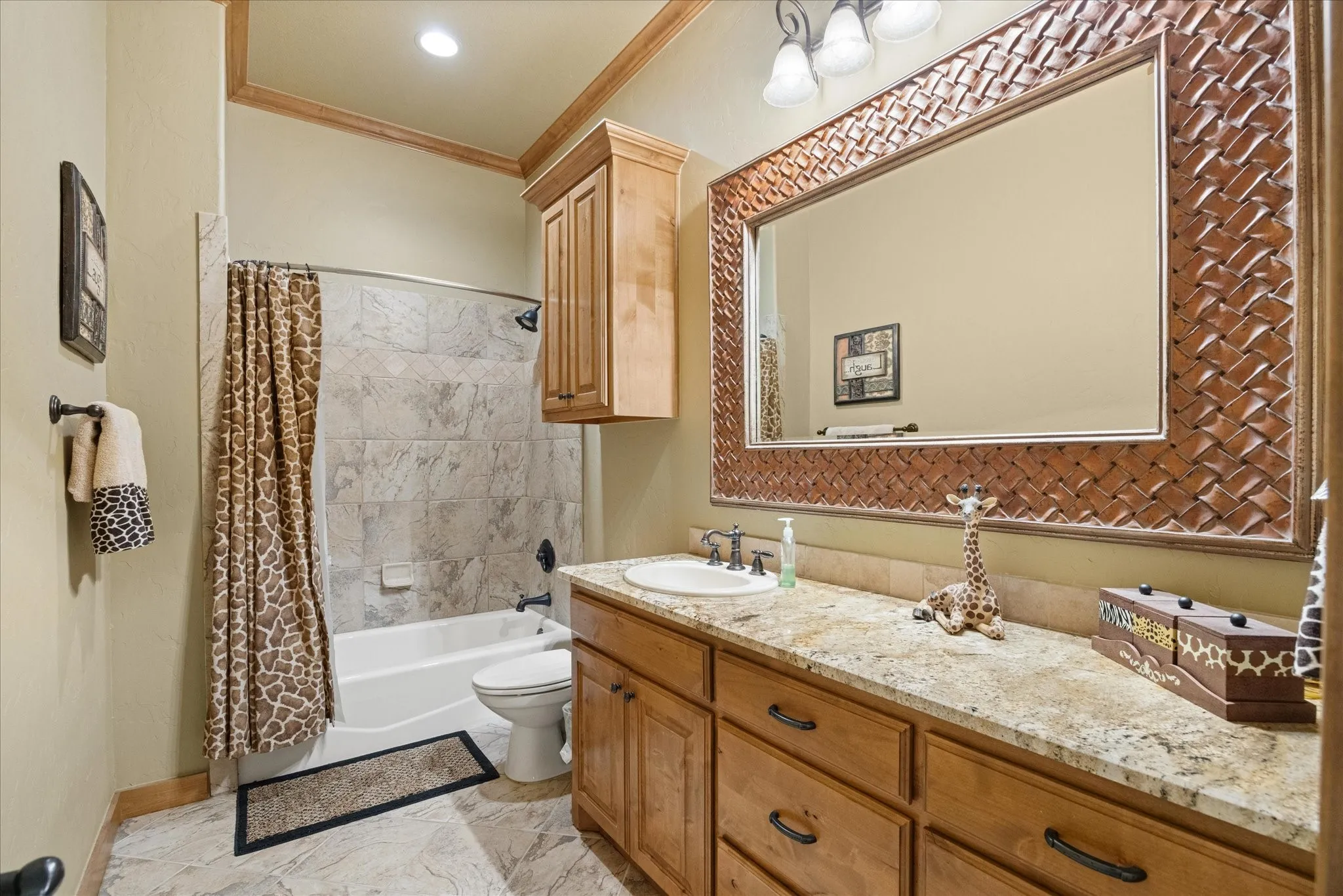 Bathroom featuring a single vanity with granite-style countertop, wood cabinetry, a large framed mirror, and a tub-shower combination with tile surround