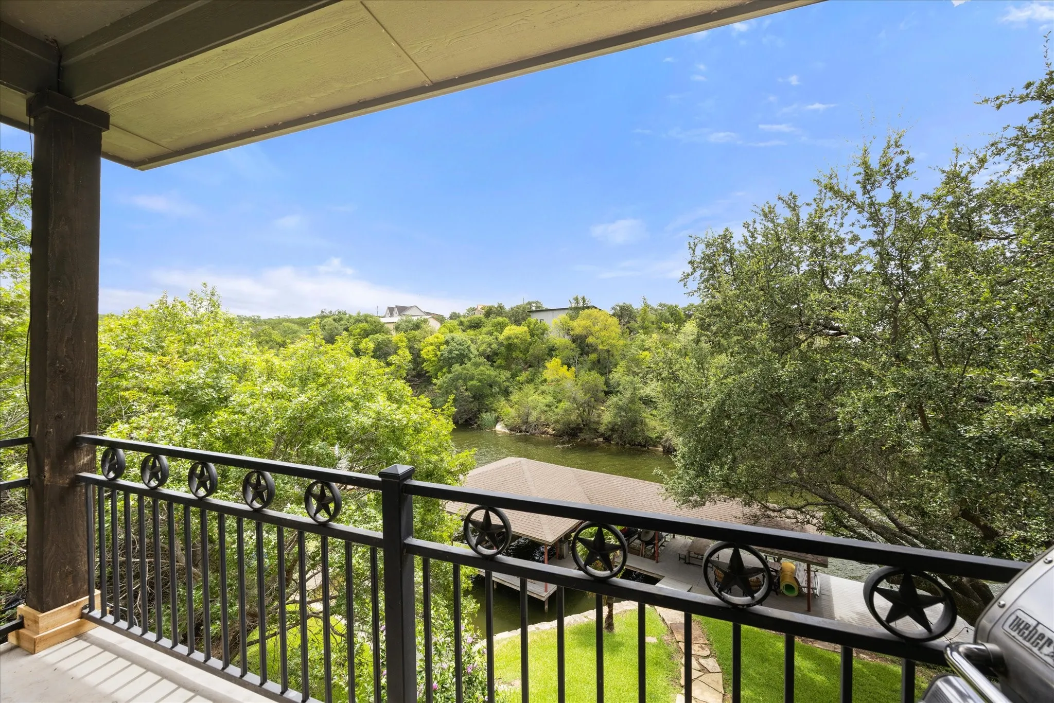 Balcony featuring a decorative black metal railing with star accents, wood-clad support columns, and a tranquil river setting with lush green trees