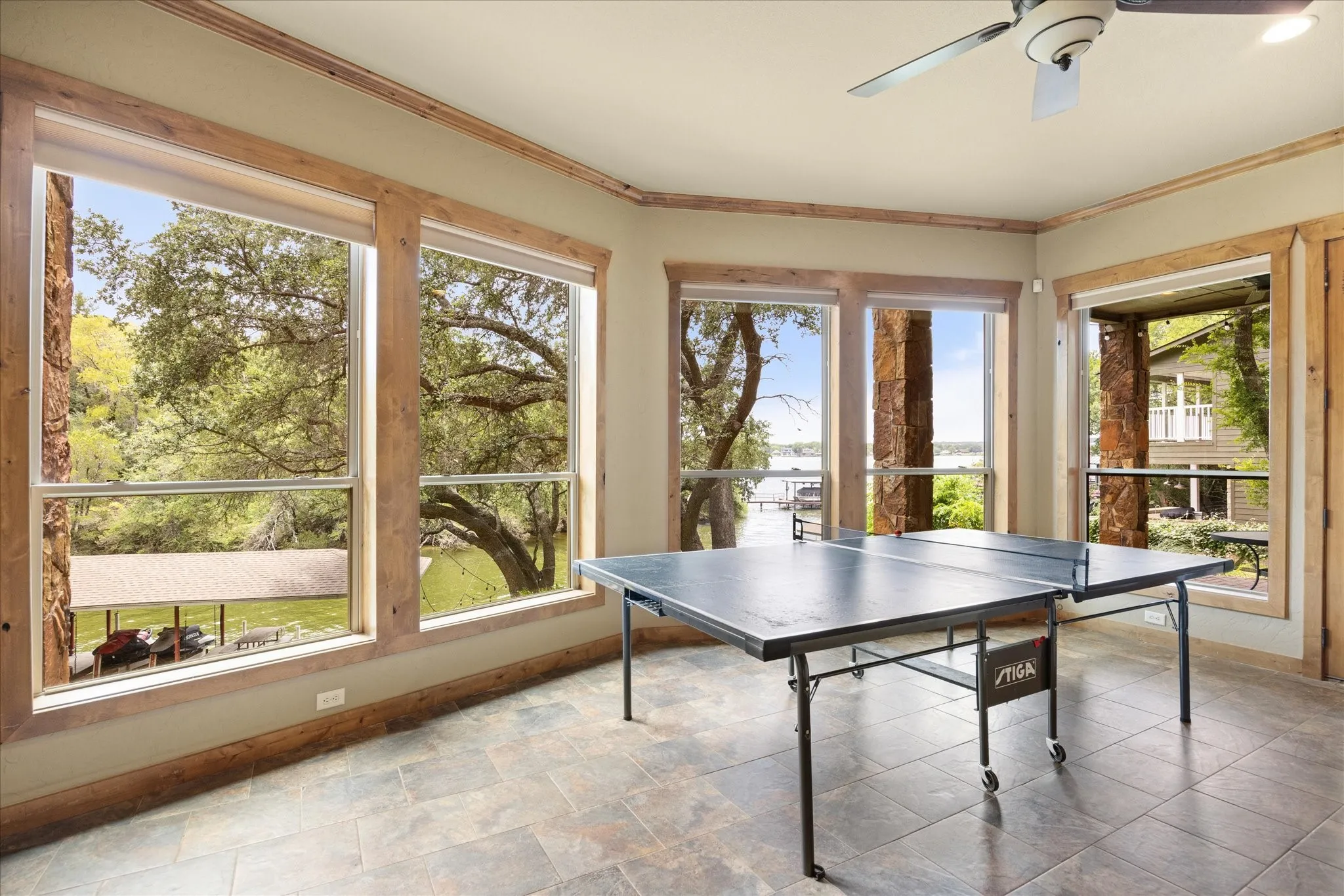 Spacious room featuring multiple large windows with natural wood trim, showcasing exterior stone columns and a waterfront backdrop