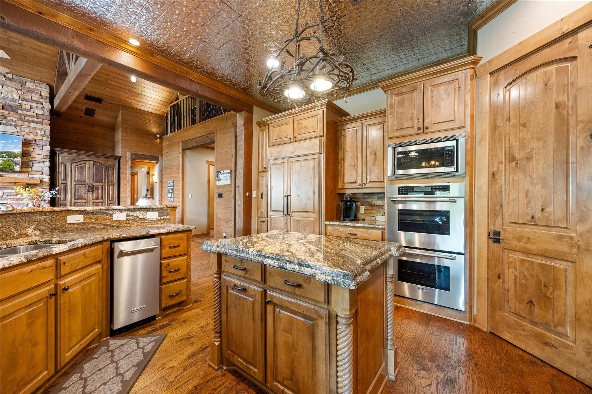 Kitchen featuring a central island, granite countertops, wood-finish cabinetry, stainless steel appliances, and a pressed tin ceiling