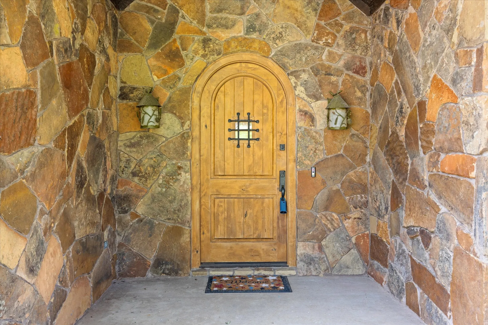 Arched wood entry door with iron grille detail, flanked by two outdoor wall lanterns