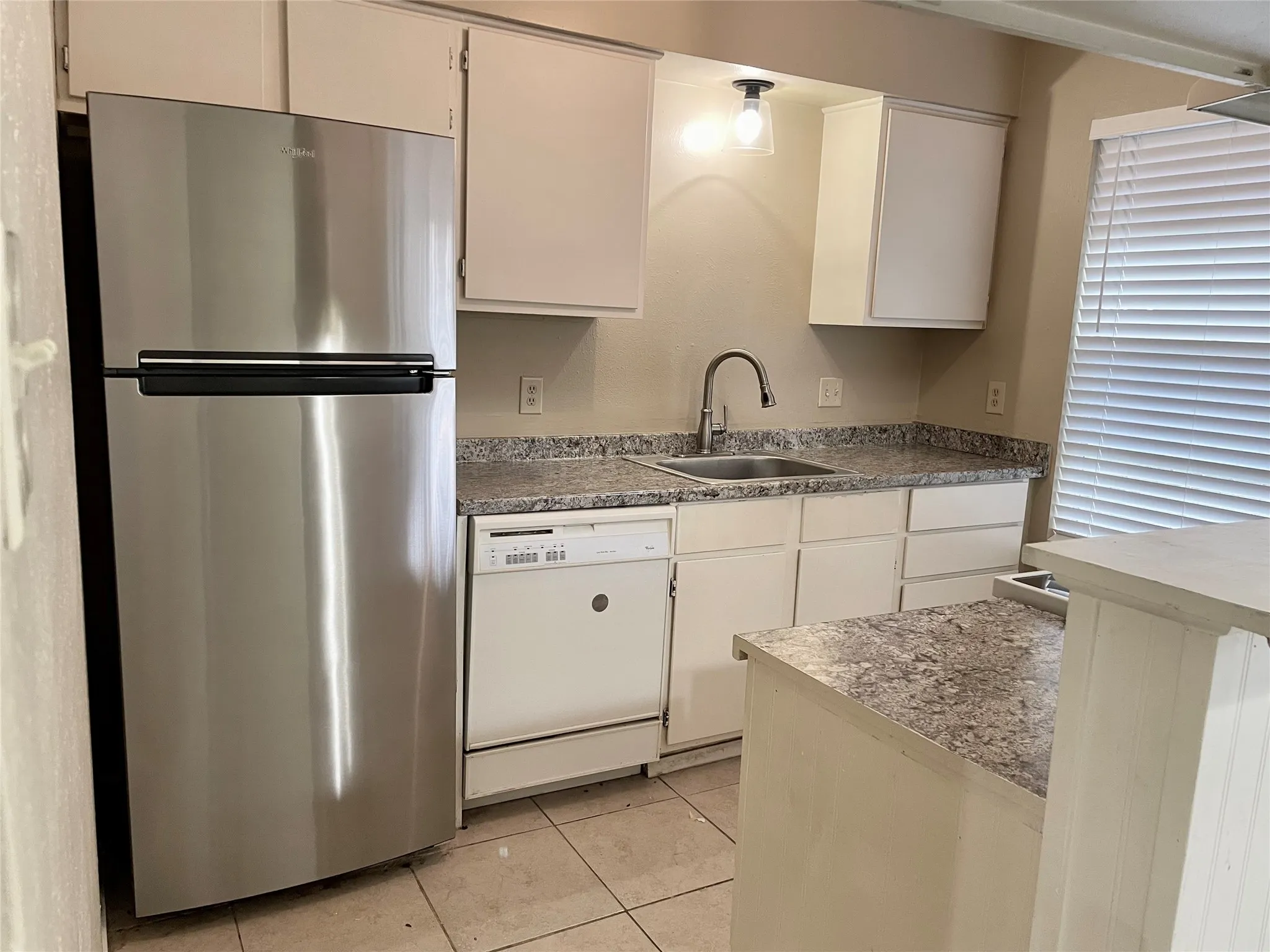 Kitchen with freestanding refrigerator, white dishwasher, light tile patterned floors, and white cabinets