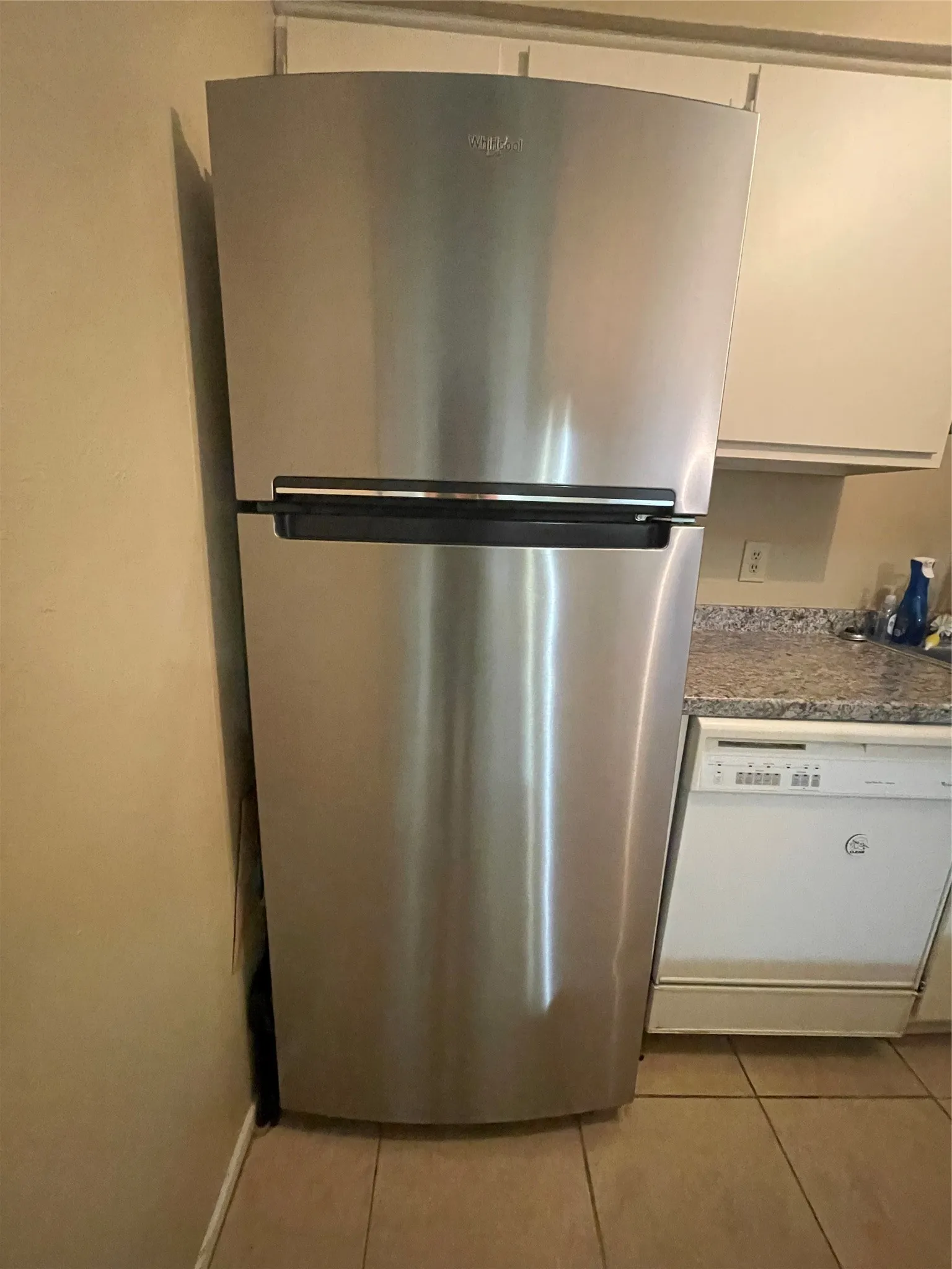 Kitchen view of freestanding refrigerator, dishwashing machine, and white cabinetry