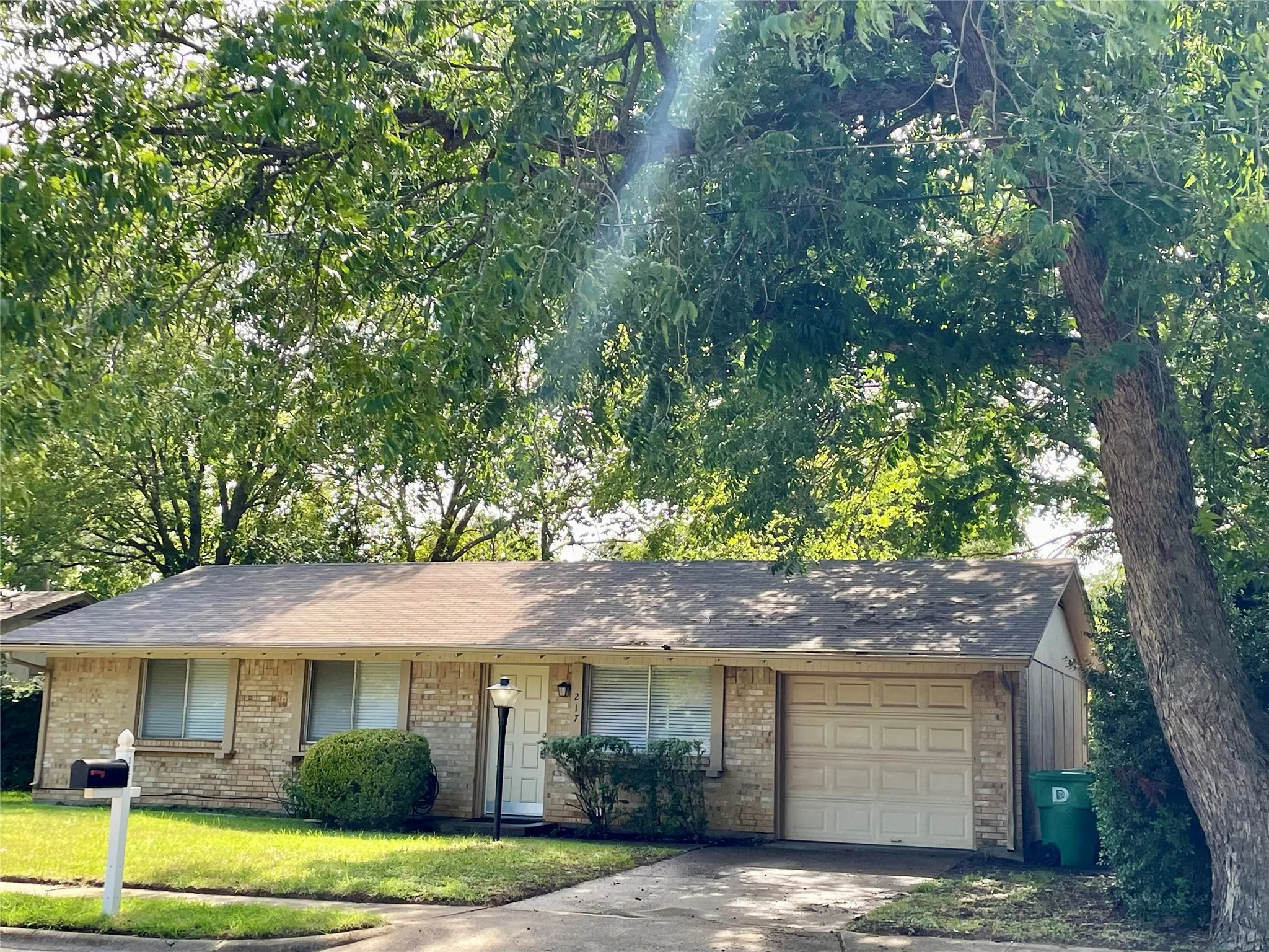 Ranch-style house with an attached garage, concrete driveway, a shingled roof, brick siding, and a front lawn