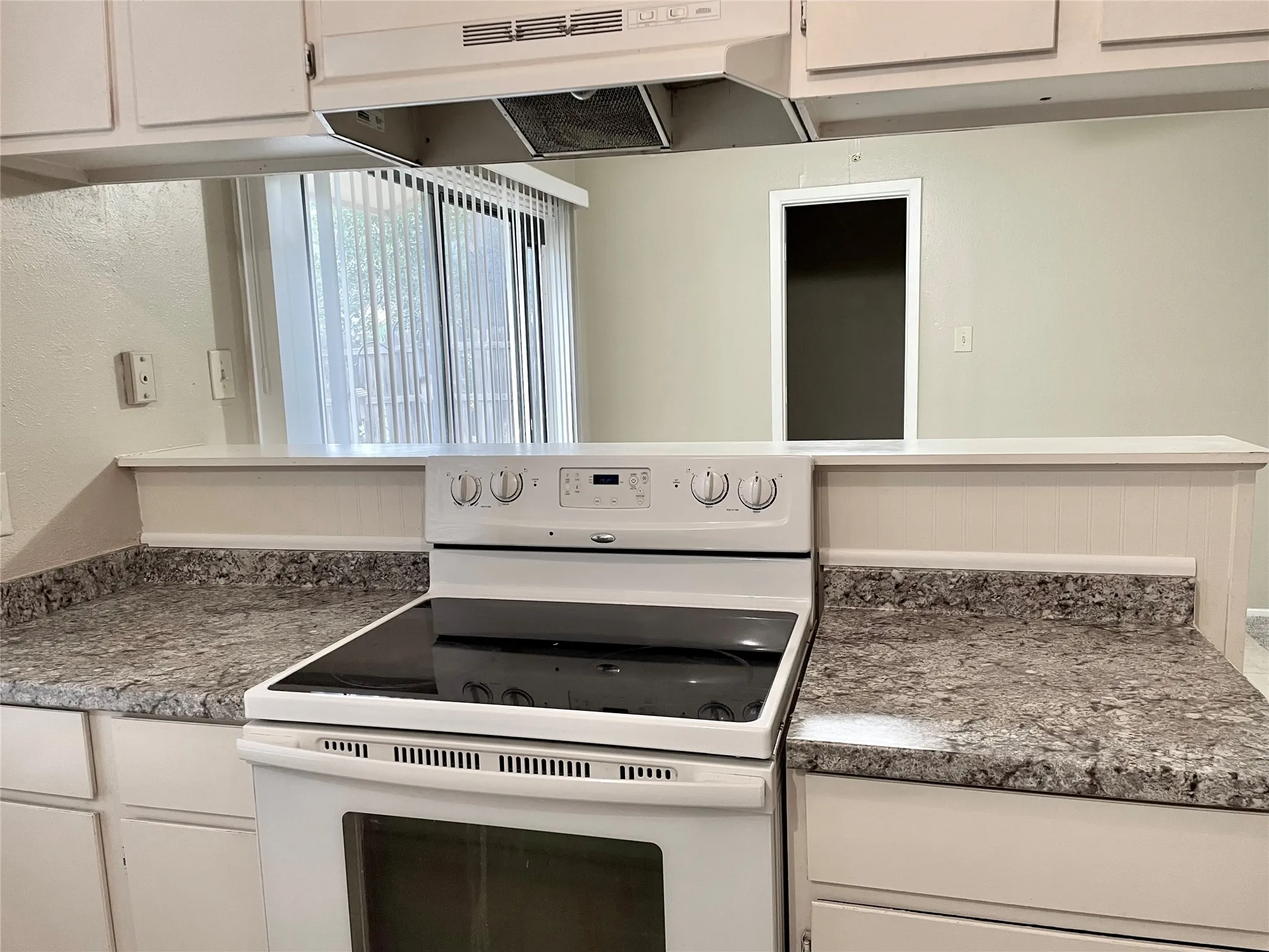 Kitchen with white range with electric cooktop, under cabinet range hood, and white cabinets