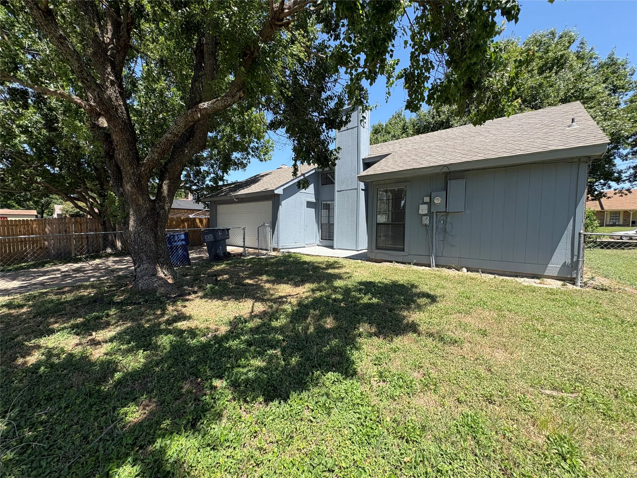 Spacious grassy yard featuring mature trees and a chain-link fence