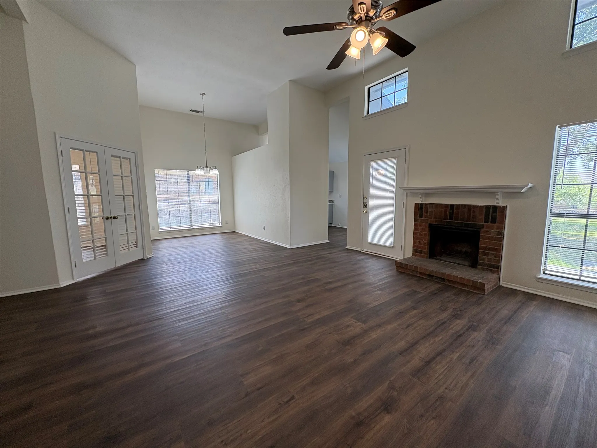 Spacious living area featuring high vaulted ceilings, wood-finish flooring, and a brick fireplace