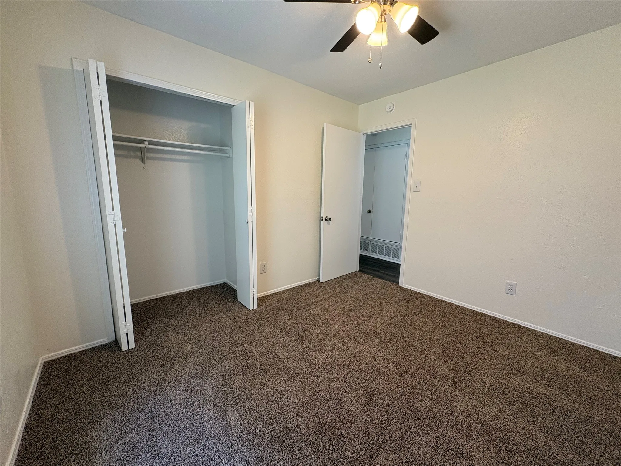 Carpeted room featuring a ceiling fan, a bi-fold door closet with dual hanging rods, and a white interior door