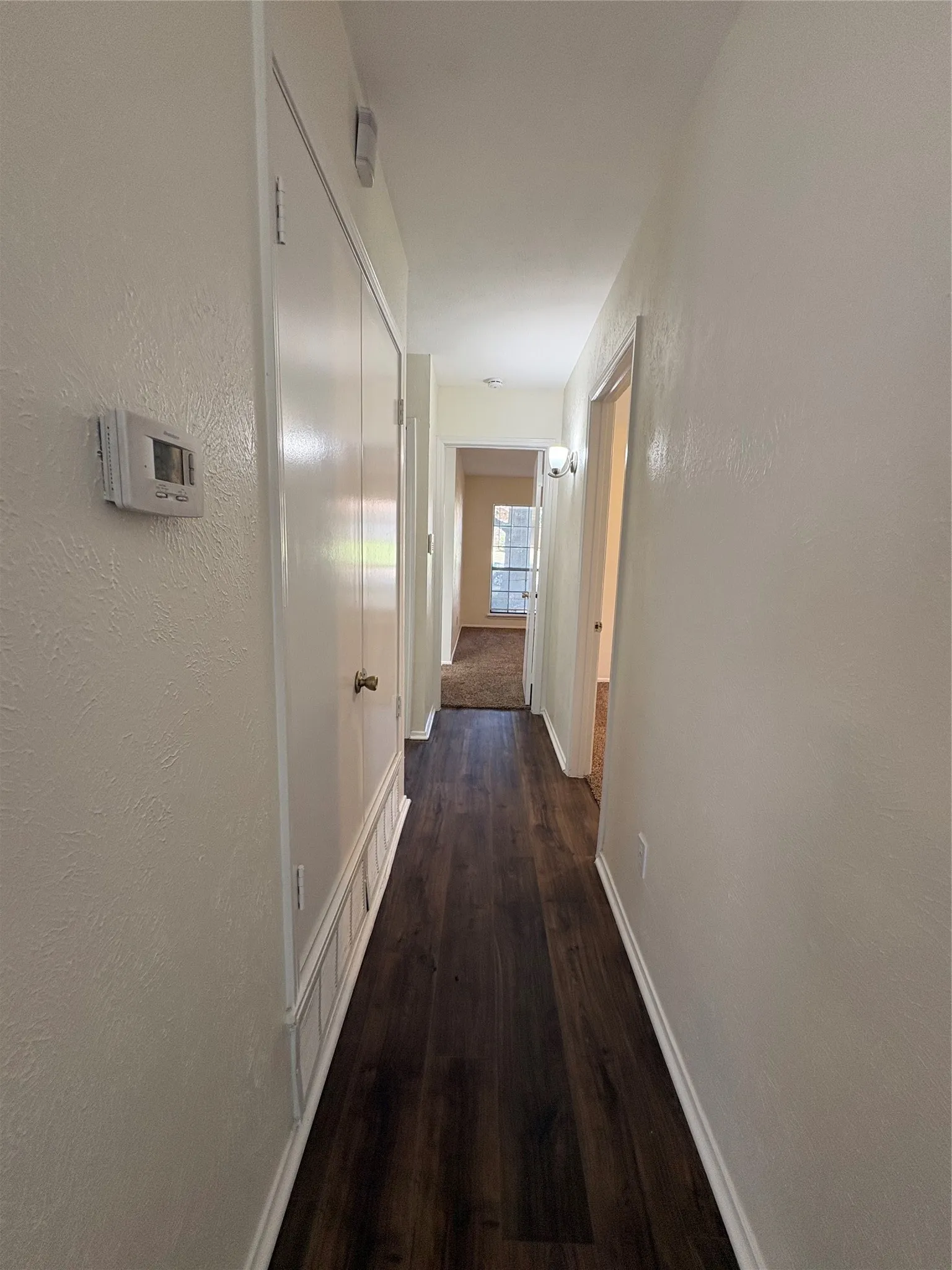 Hallway with dark wood-finish flooring, white baseboards, and light neutral wall paint