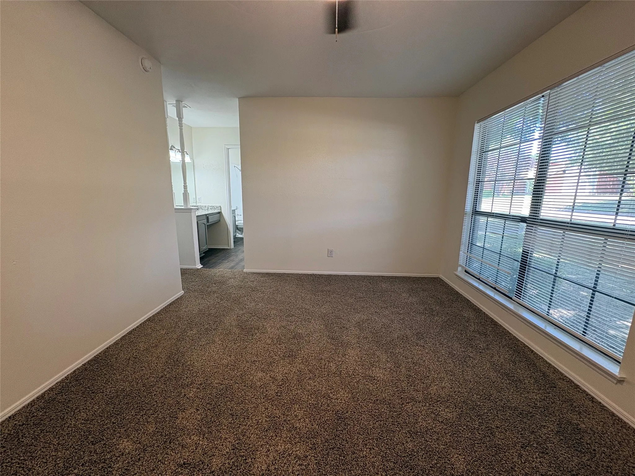 Carpeted room featuring a large window with blinds, neutral wall paint, and white baseboards