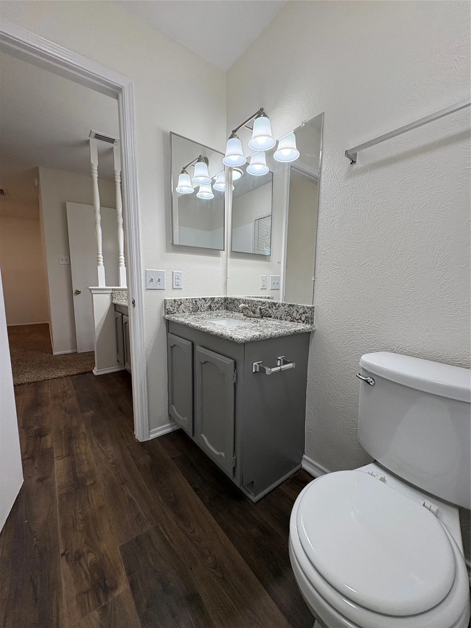 Bathroom featuring a dark wood-finish floor, gray vanity with a light speckled countertop, and a white toilet