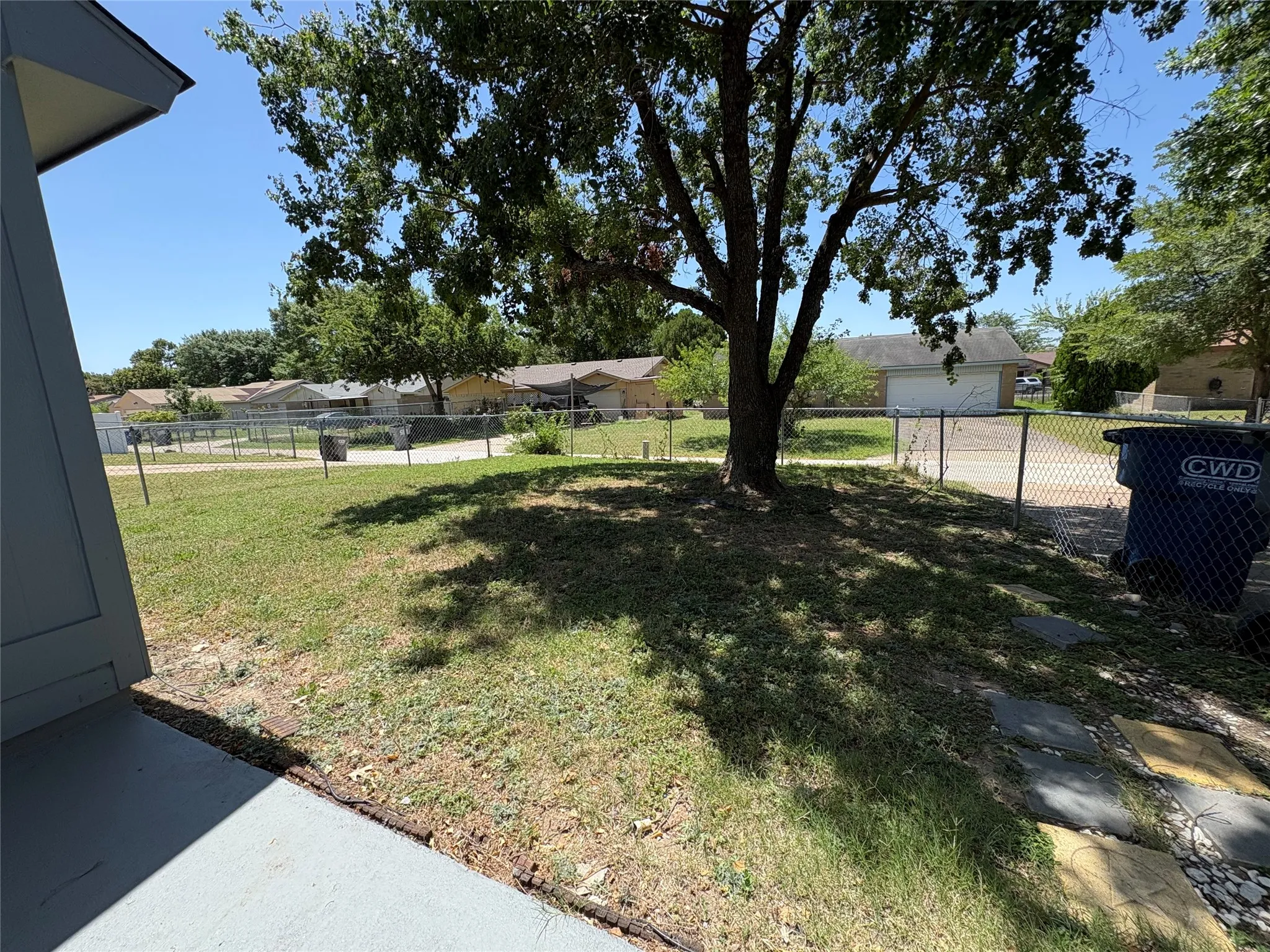 Expansive fenced yard featuring a mature shade tree and stepping stone pathway