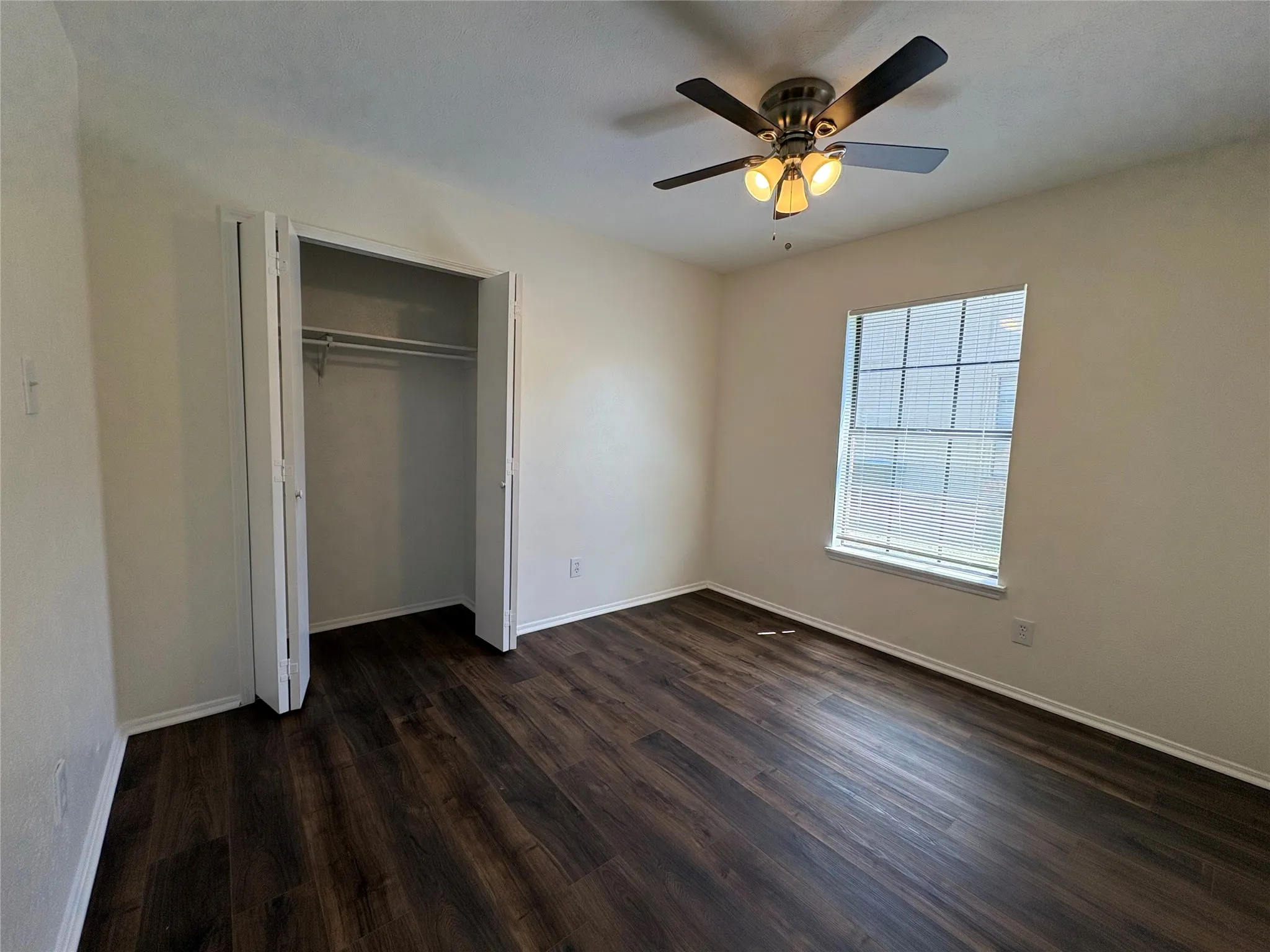 Room featuring wood-finish flooring, a window with blinds, and a built-in closet with bi-fold doors