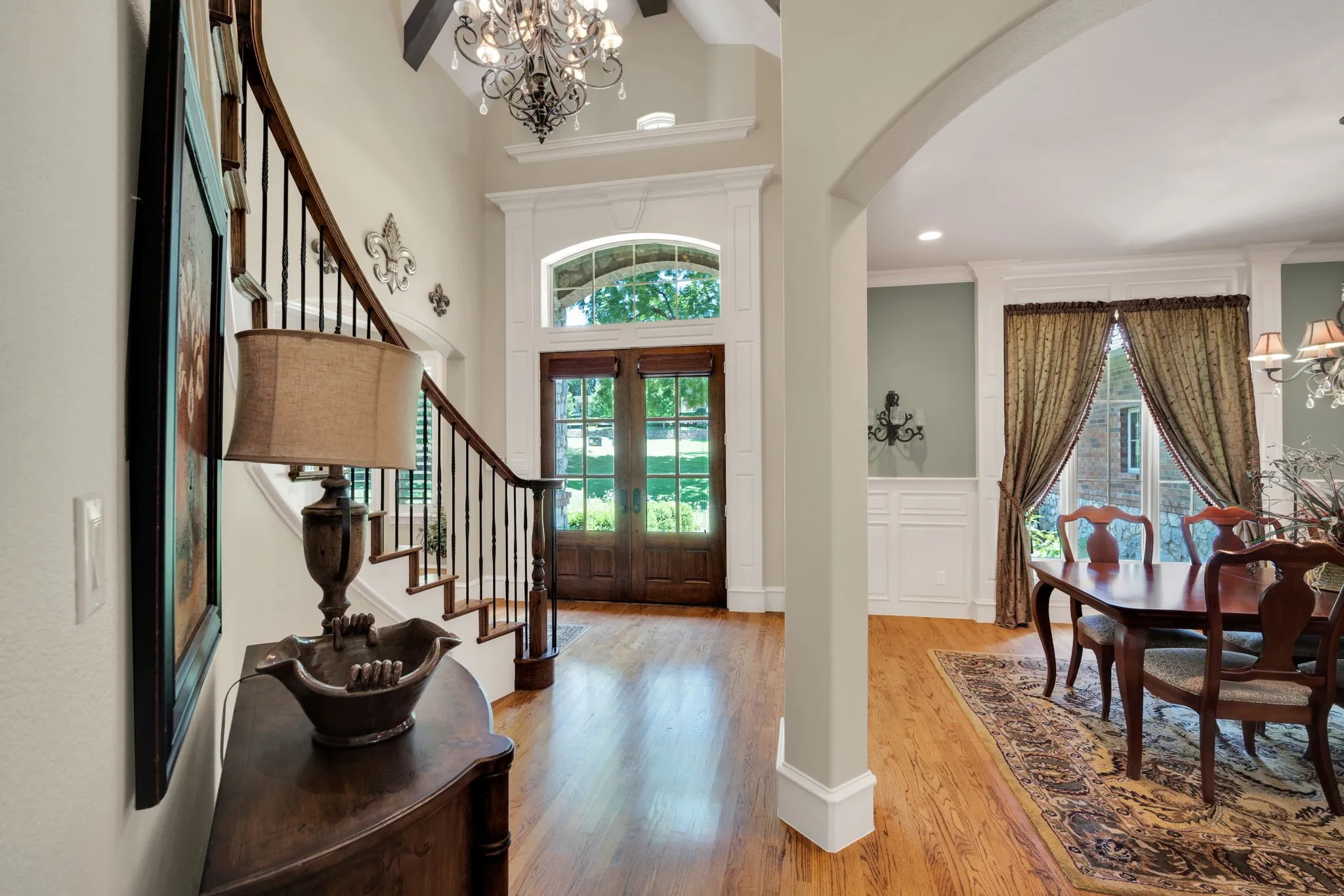 Grand foyer featuring wood-finish flooring, a detailed staircase with wrought iron balusters, and a double-door entry with an arched transom