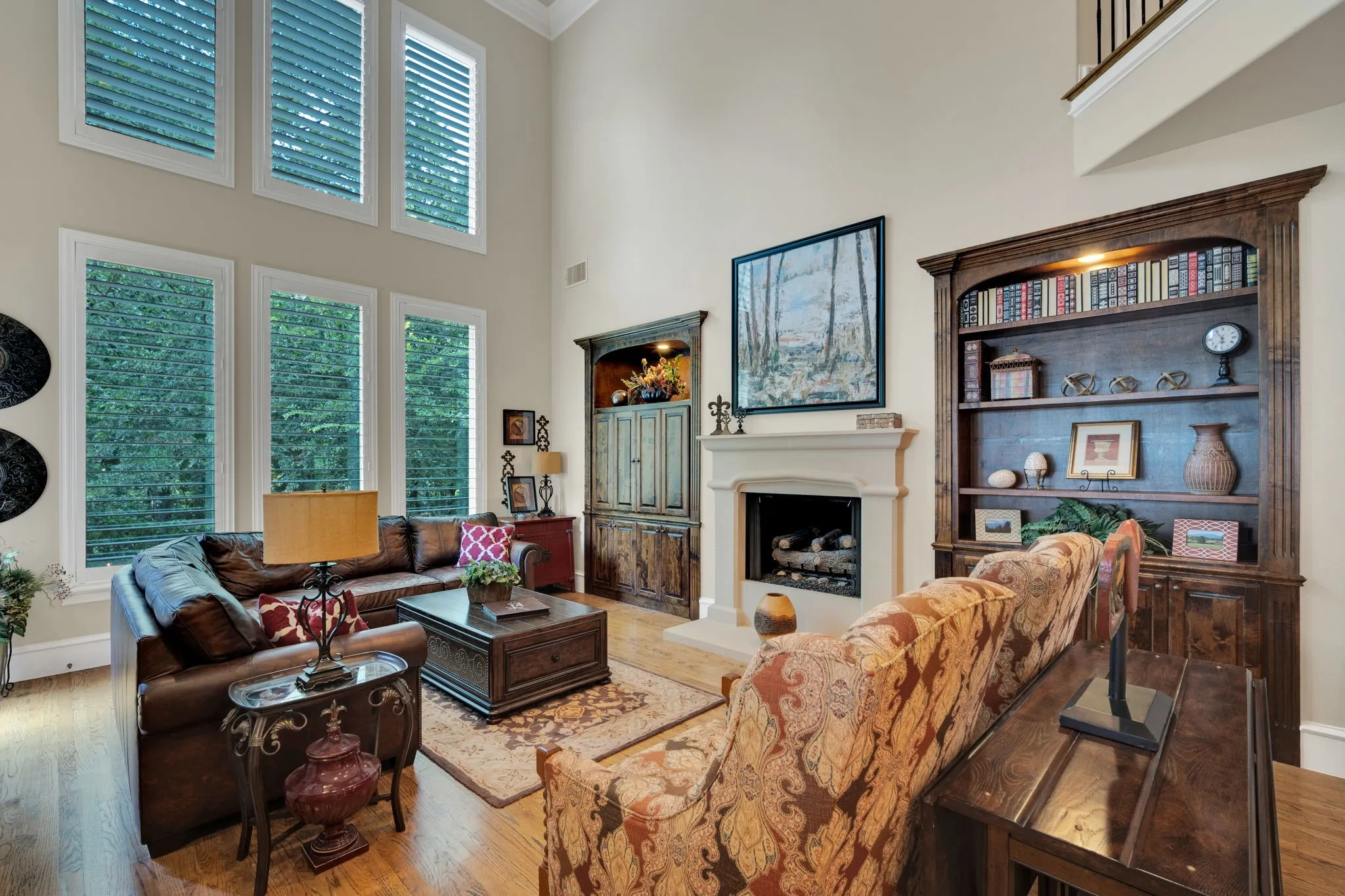 Vaulted living space featuring wood-finish flooring, a stone-surround fireplace, and custom built-in shelving