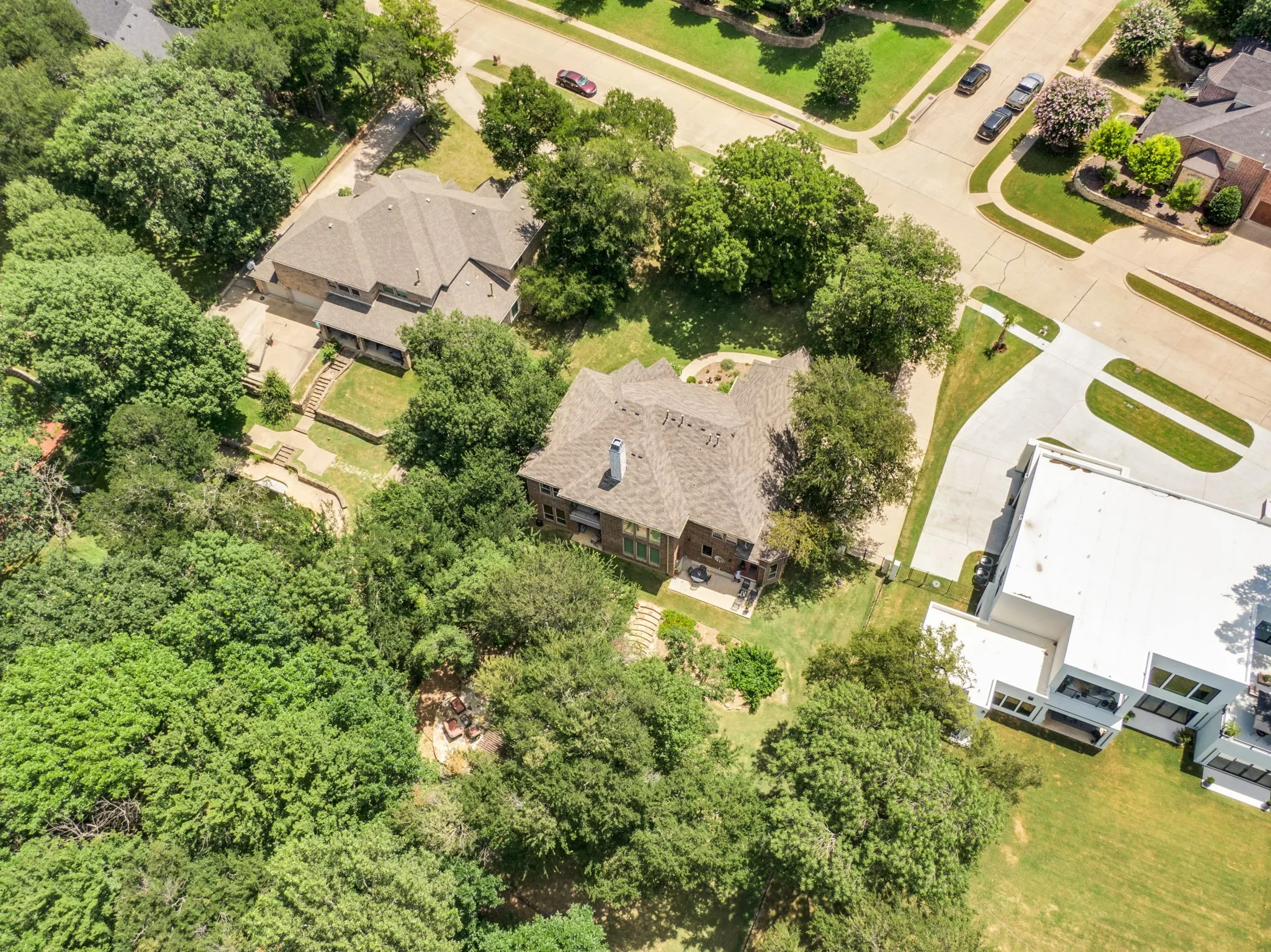 Brown shingle roof home with a stone chimney, surrounded by mature trees and manicured landscaping