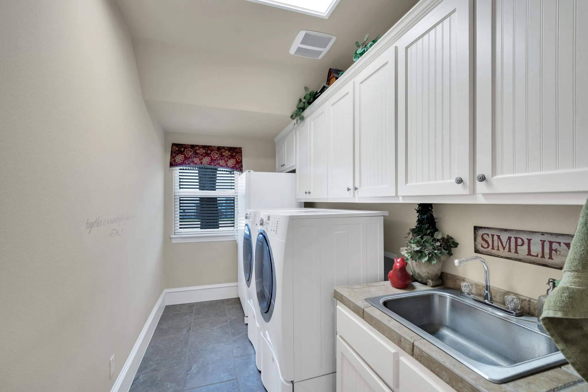 Dedicated utility room featuring abundant white shaker-style cabinetry, a stainless steel sink, and a countertop space