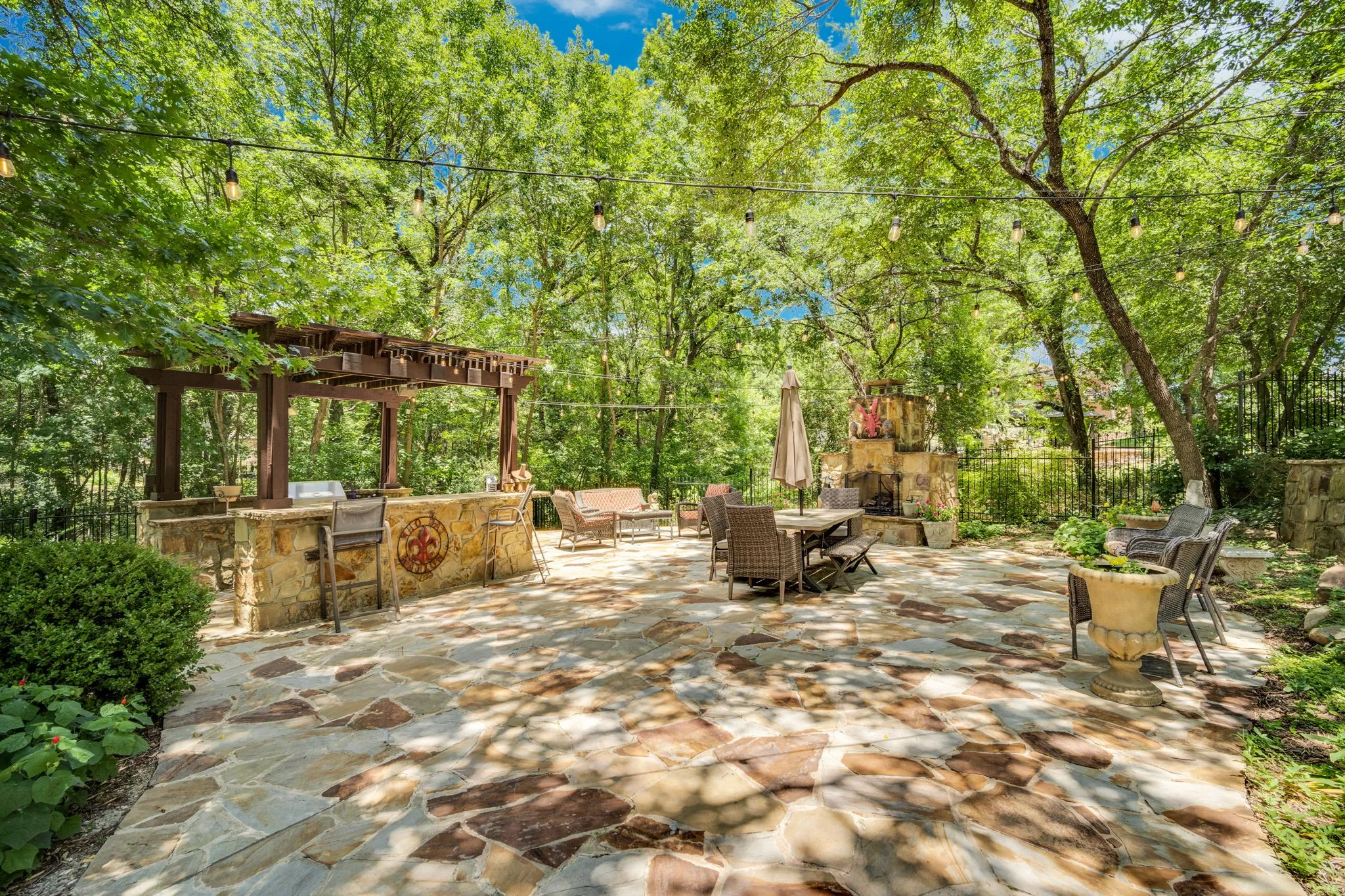 Expansive flagstone patio featuring a built-in outdoor kitchen with a pergola, a stone-clad outdoor fireplace, and string lighting