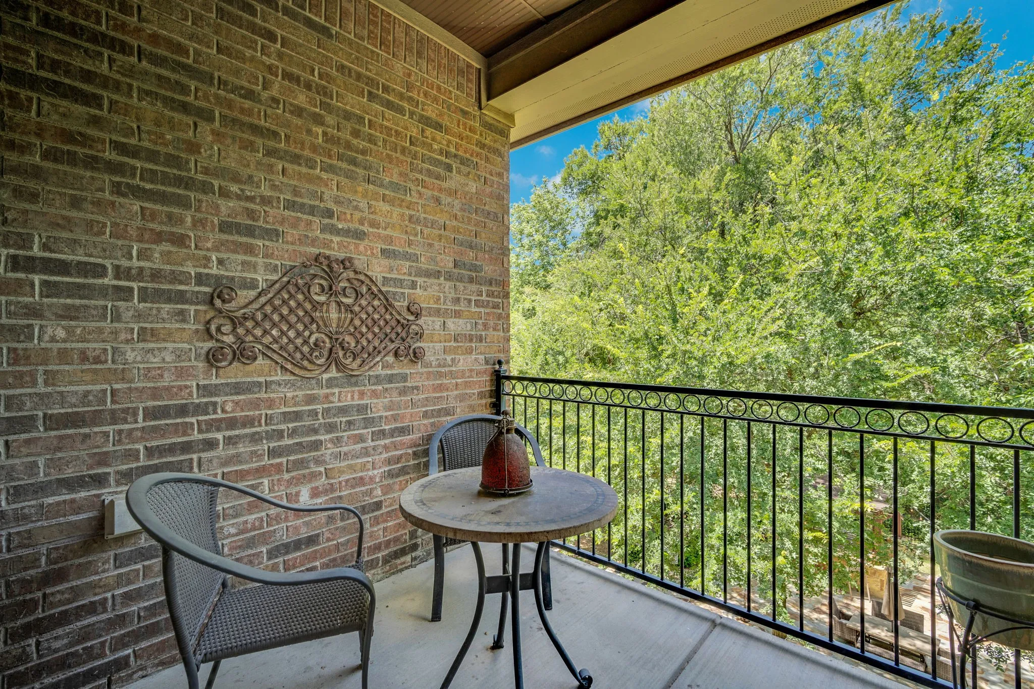 Outdoor balcony featuring a brick exterior wall, dark metal railing with decorative accents, and a light-colored concrete floor