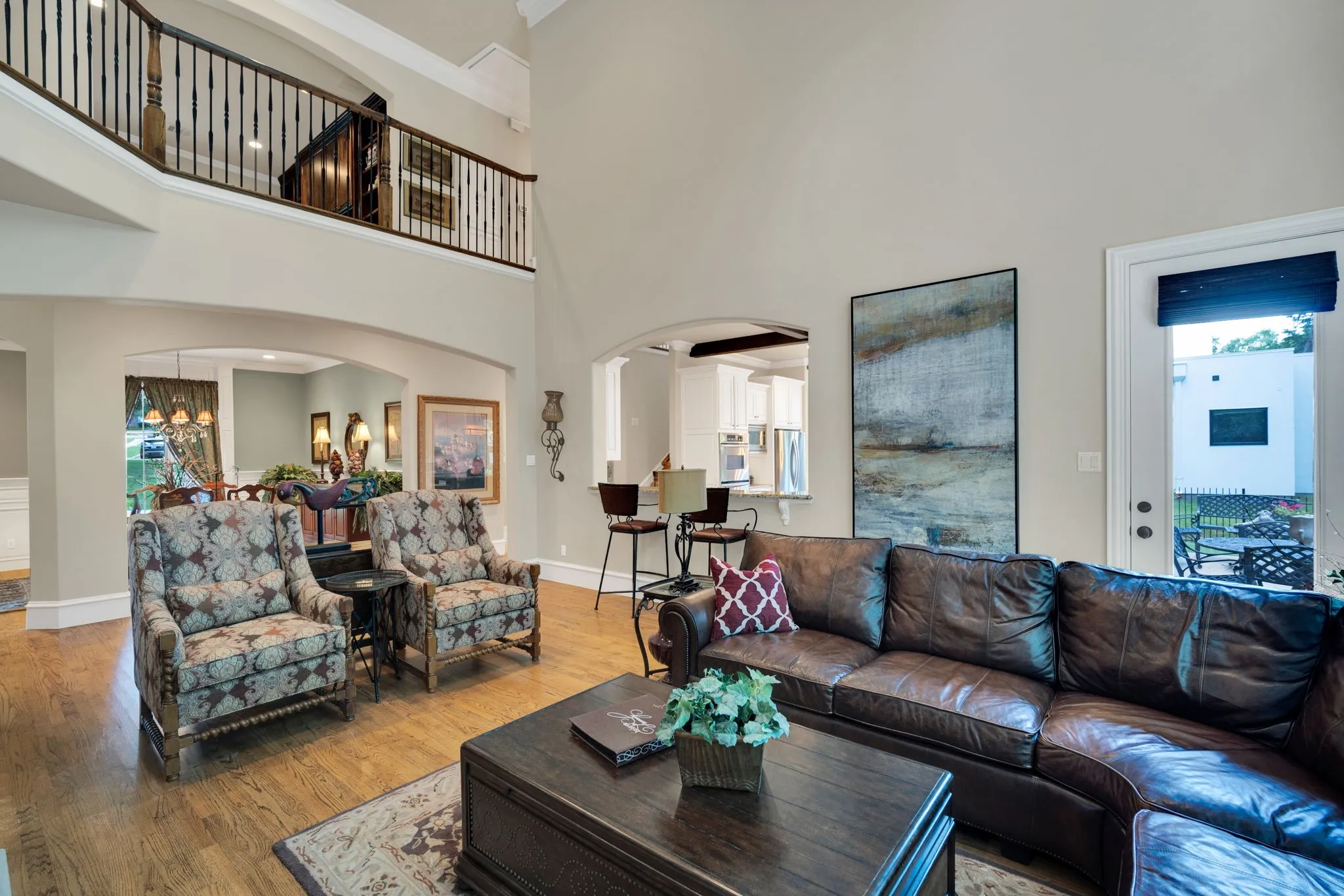 Two-story living area featuring wood-finish flooring, a wrought iron and wood staircase, arched doorways, a built-in bar, and a glass-paneled door