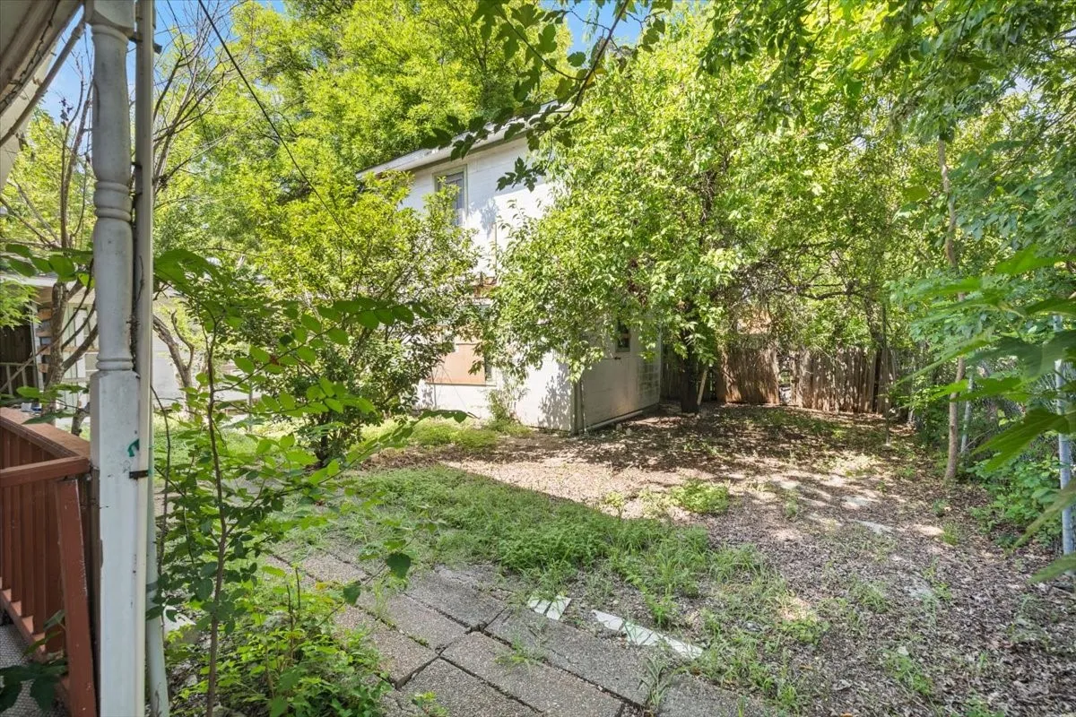 Expansive rear yard featuring mature trees, a partial privacy fence, and a concrete paver path