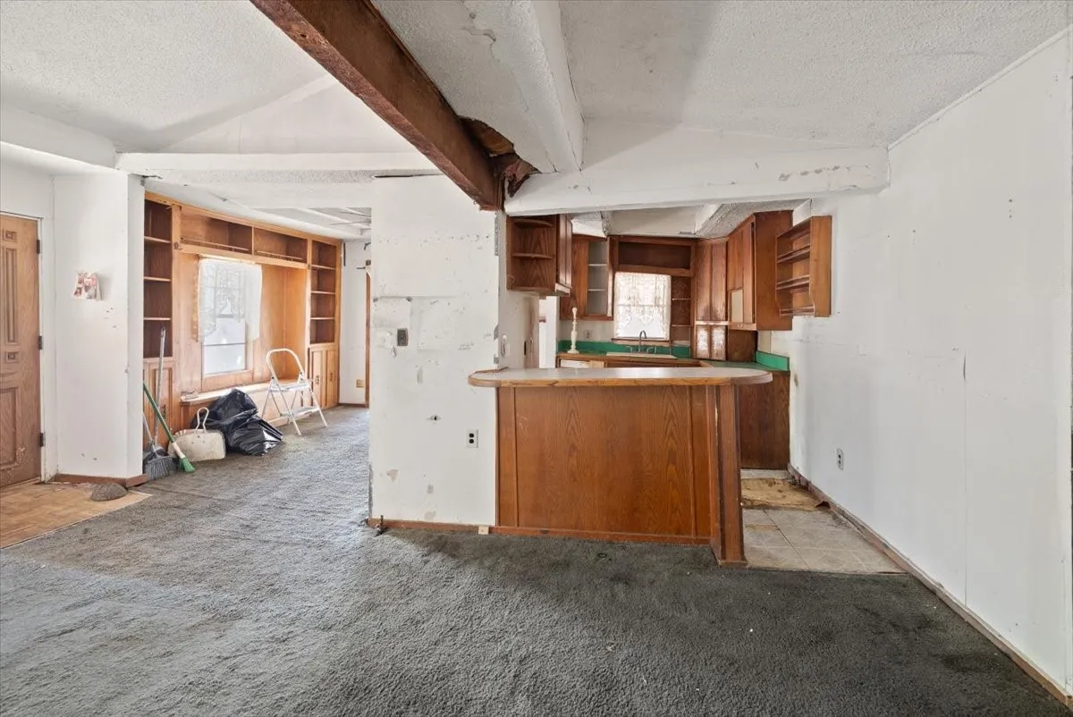 Open-concept living area featuring exposed ceiling beams and a built-in kitchen peninsula