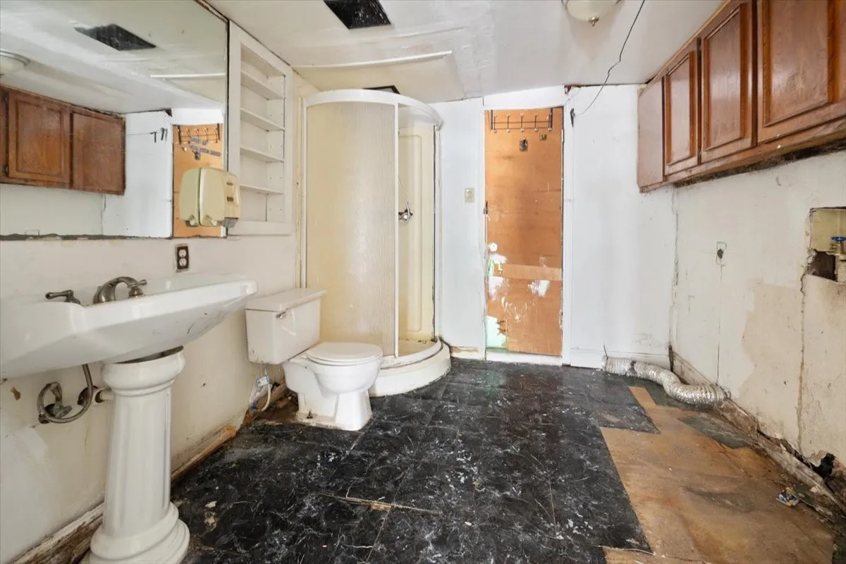 Pedestal sink with exposed plumbing, white toilet, and enclosed shower stall