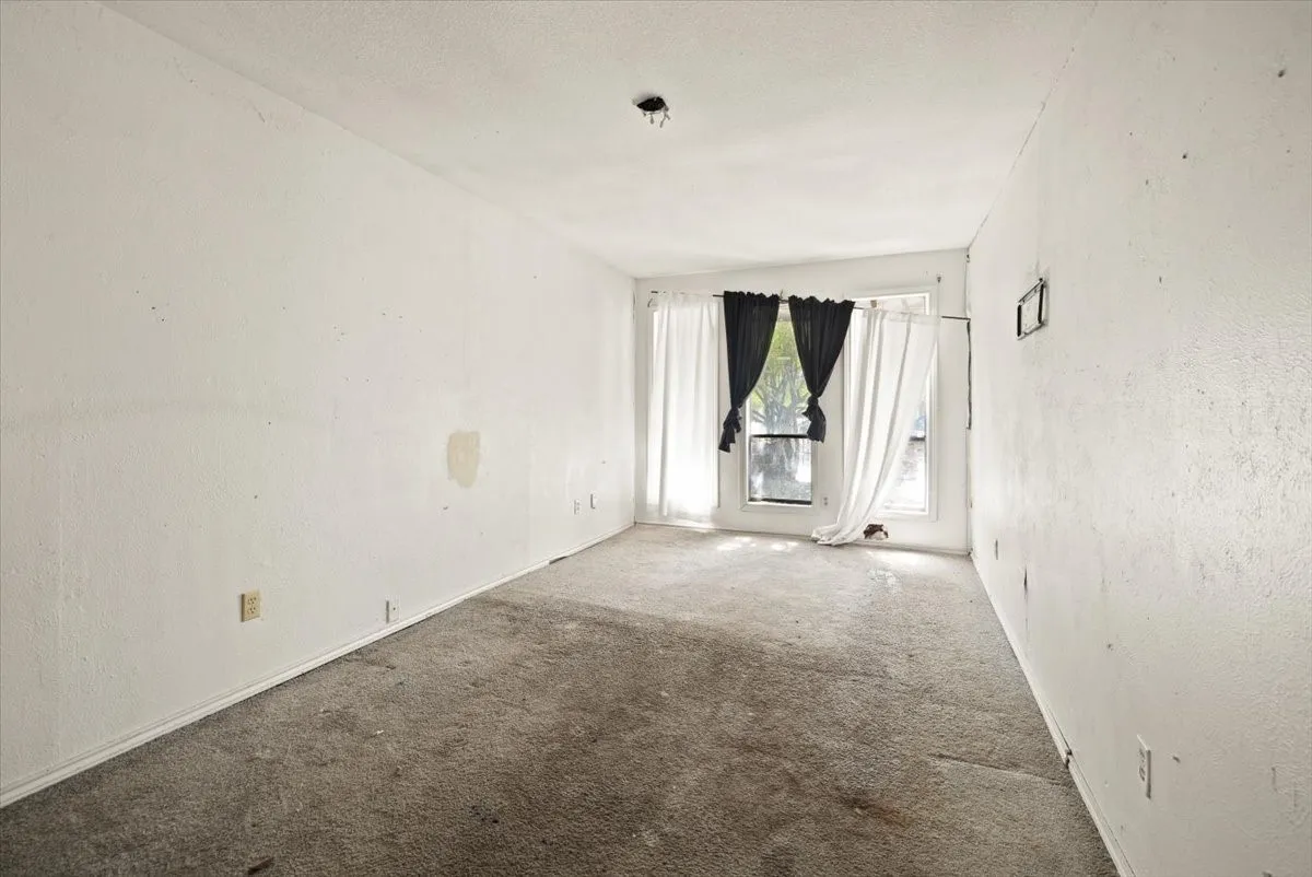 Carpeted room with a textured ceiling, featuring a window with a sill and baseboard trim