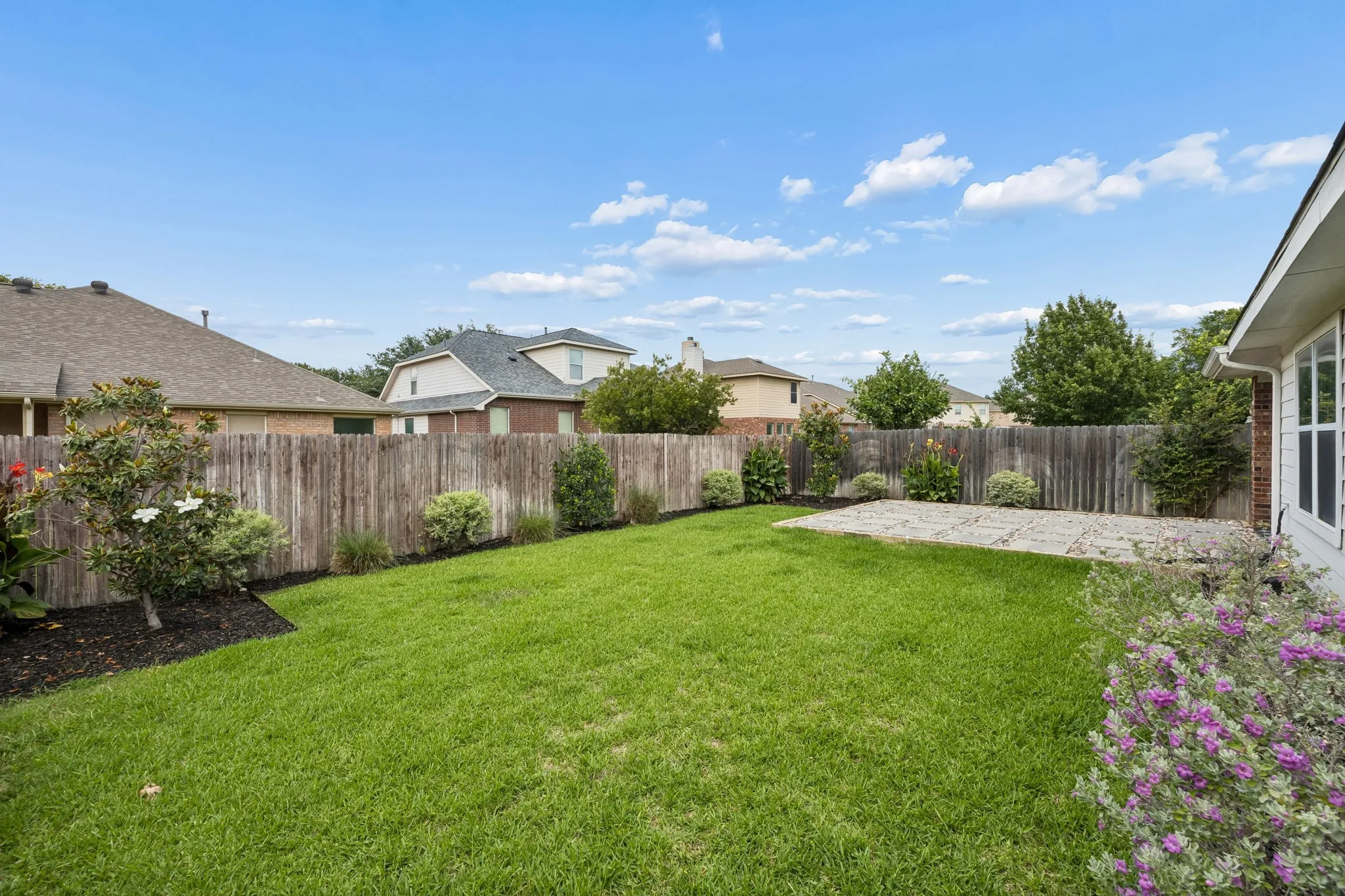 Backyard is fenced and landscaped, with open grass area.