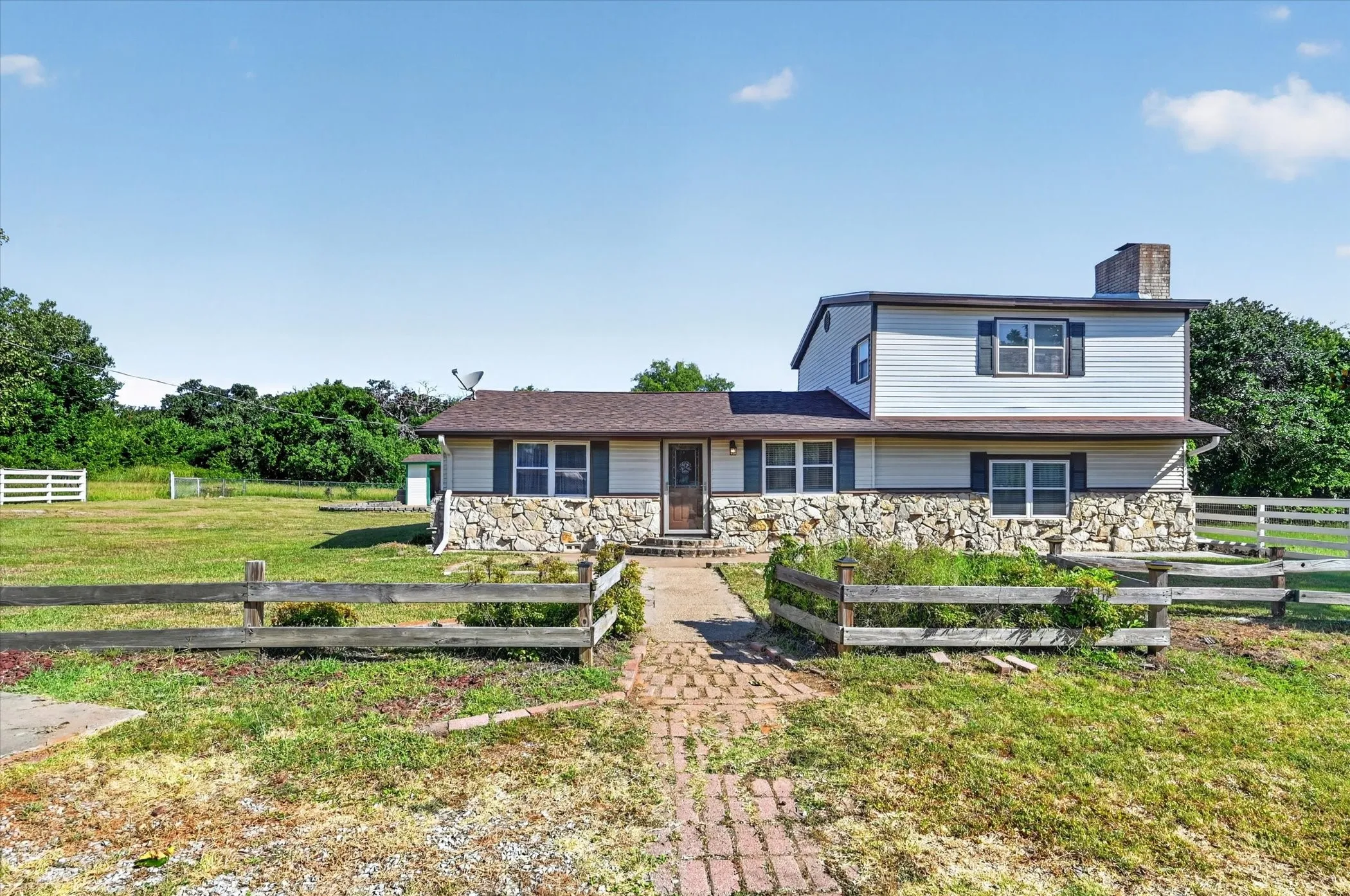 Split-level residence featuring a stone and siding exterior, a brick pathway, and a brown shingle roof