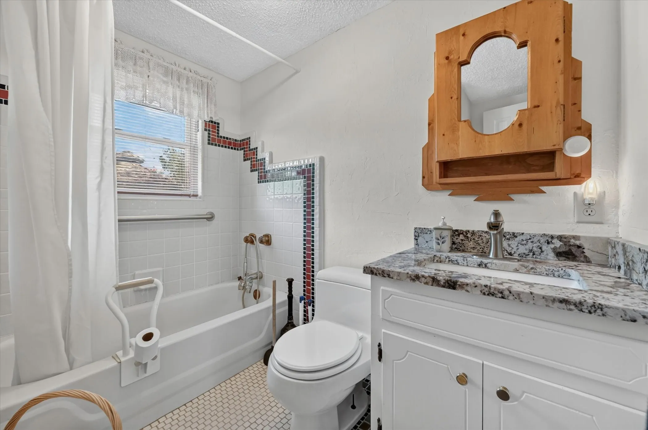 Bathroom featuring a white bathtub, a window with blinds, a vanity with a stone countertop, a built-in sink, and a wooden medicine cabinet