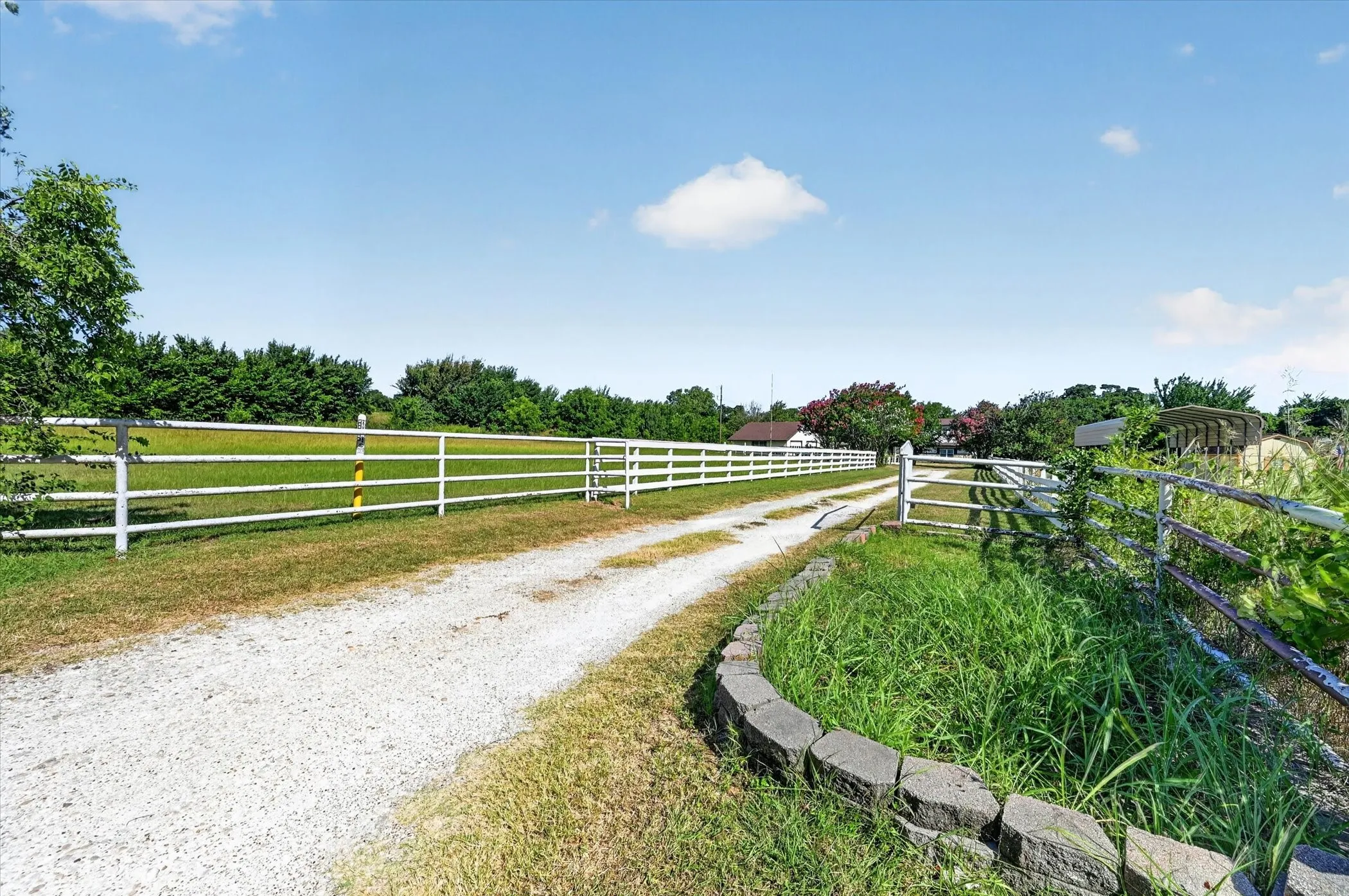Gravel driveway entrance with white fencing and a curved stone-edged planter