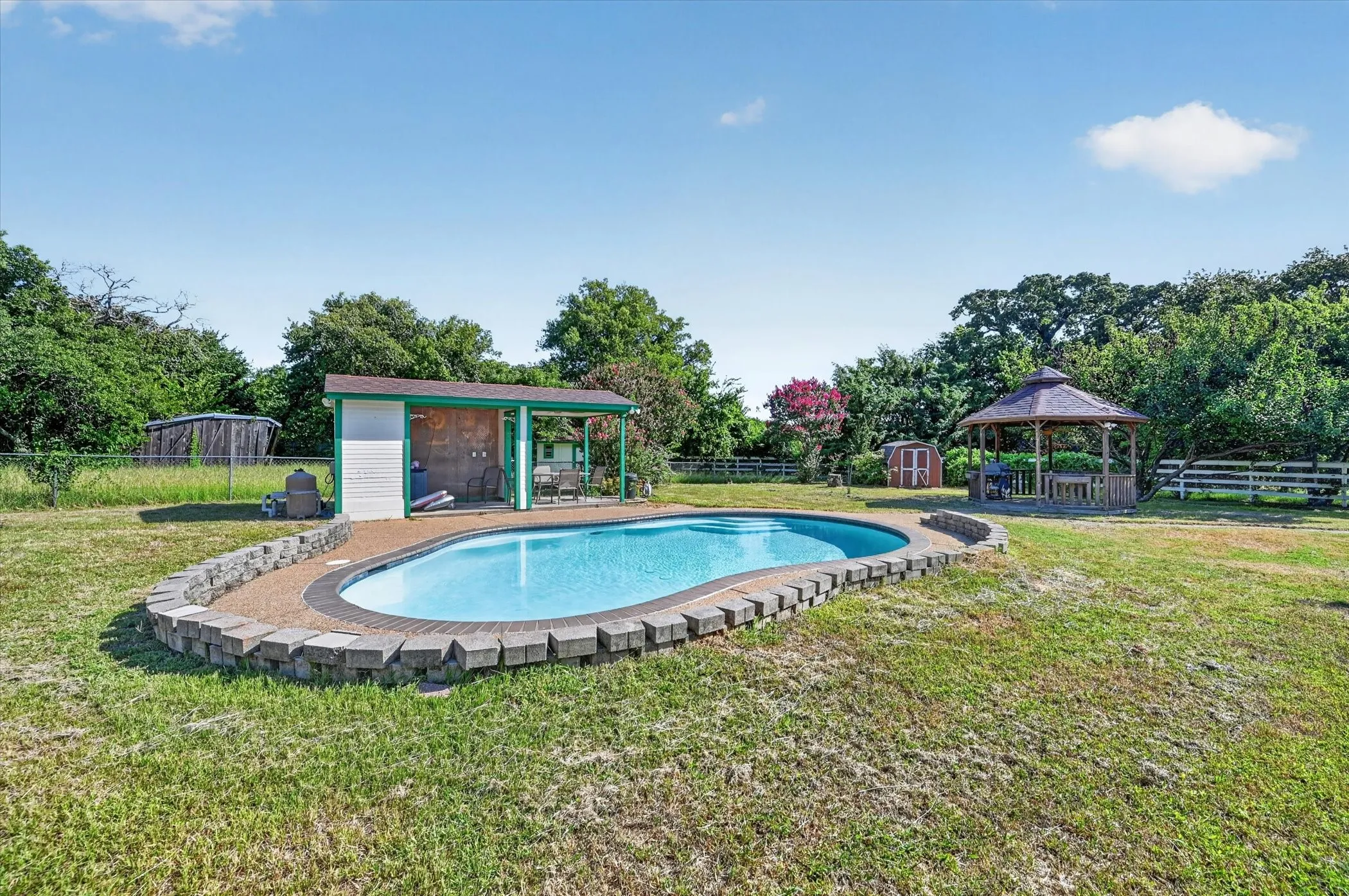 Kidney-shaped swimming pool featuring a stone block surround and pebble-finish decking