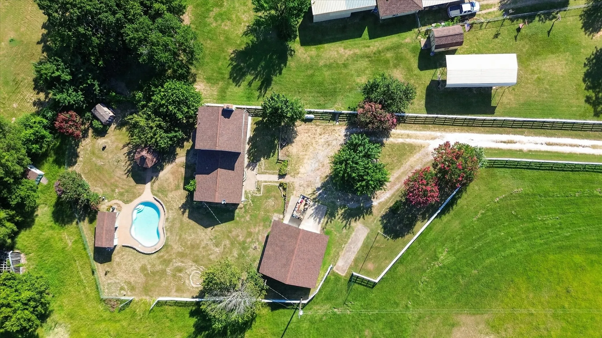 Aerial perspective showcasing a residential property with a freeform swimming pool, a main residence with a brown shingle roof, and an additional detached structure