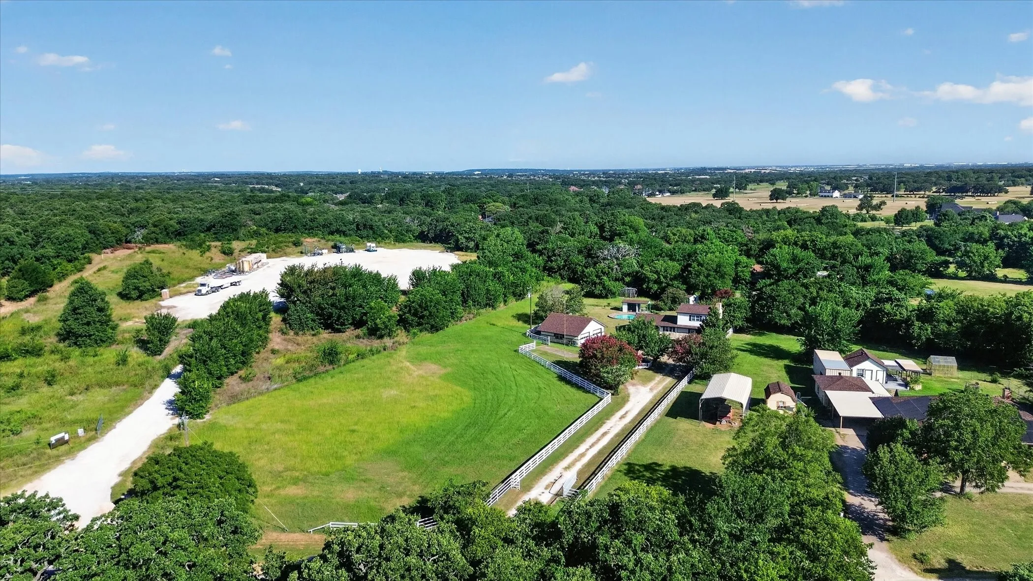 Expansive property featuring a gravel driveway, multiple outbuildings, and significant acreage surrounded by mature trees