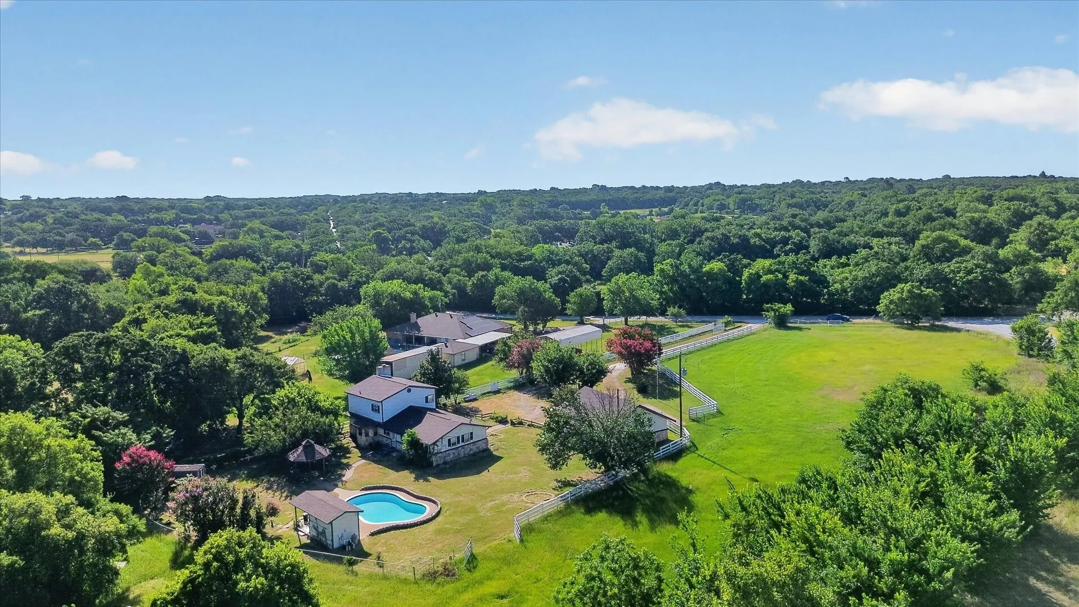Expansive property featuring multiple structures, a free-form swimming pool, and a white picket fence