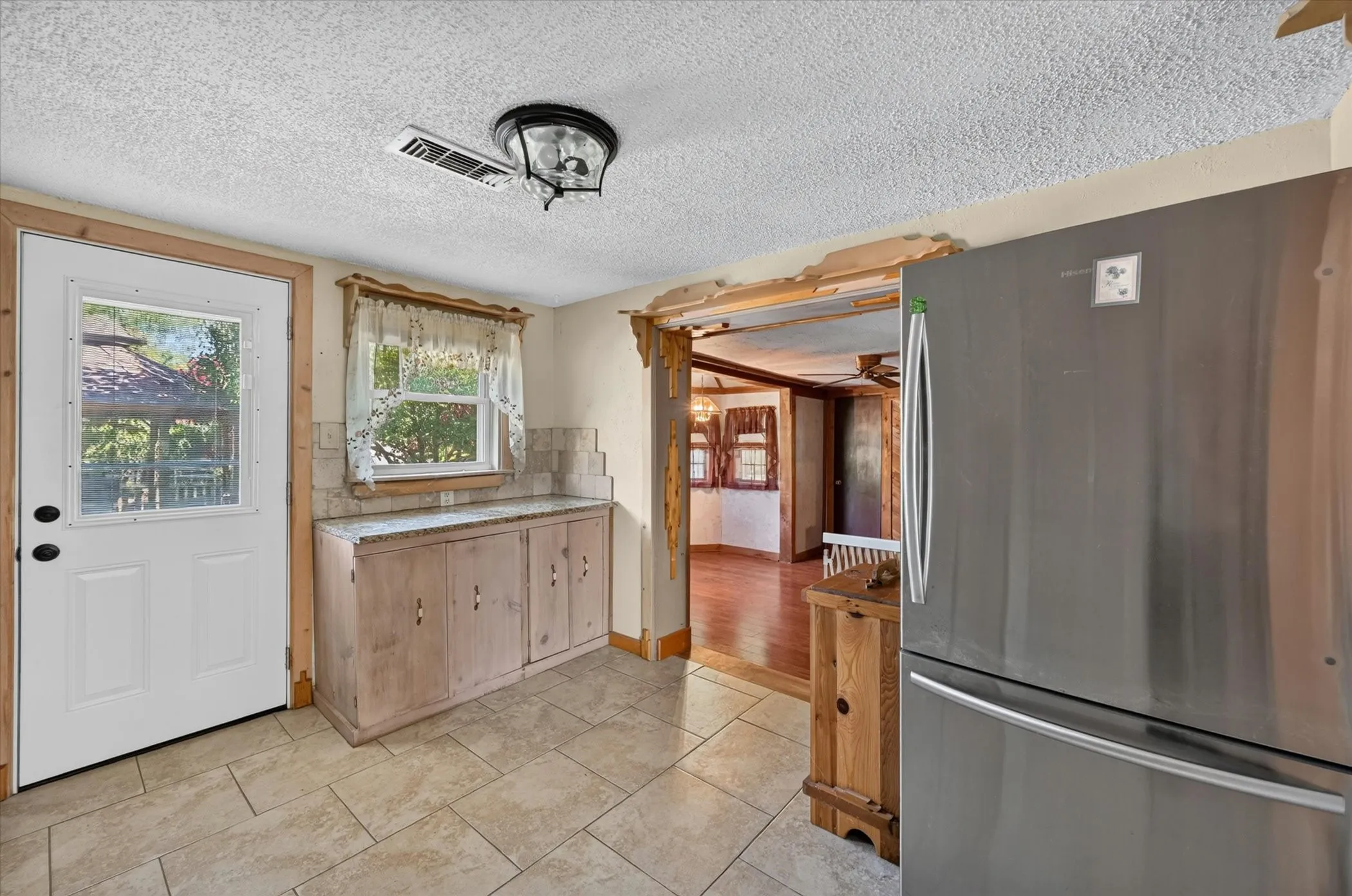 Kitchen area featuring tiled flooring, built-in wooden cabinetry with a light-colored countertop, and a window with trim