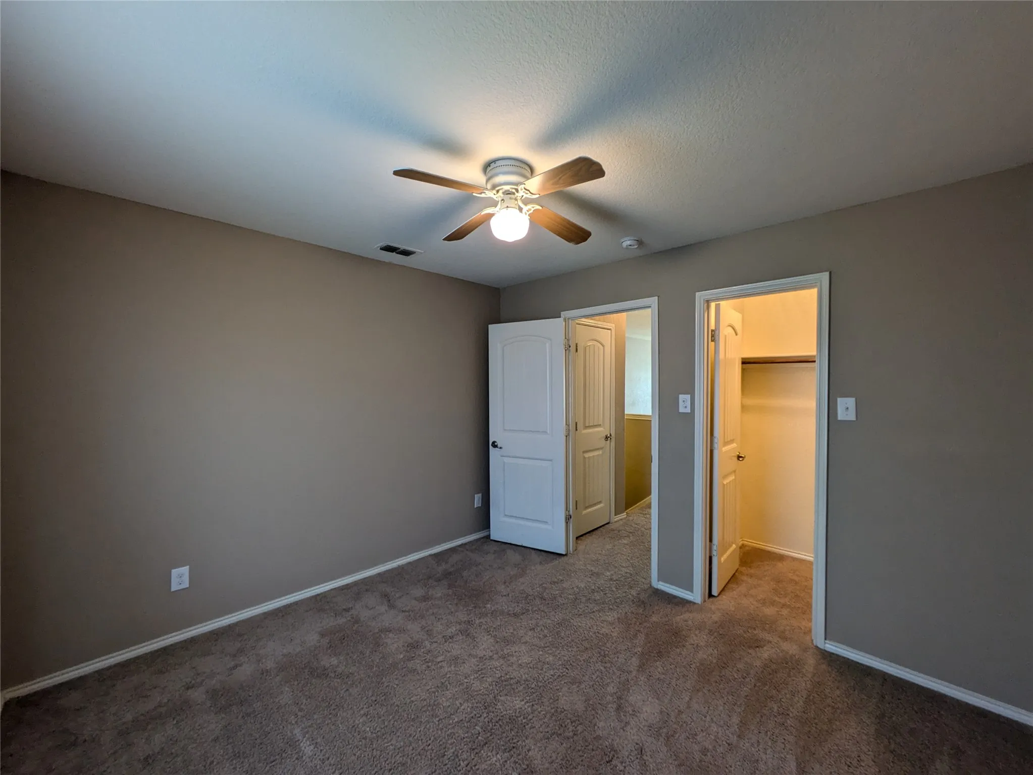 Unfurnished bedroom featuring ceiling fan, a textured ceiling, a walk in closet, a closet, and carpet floors