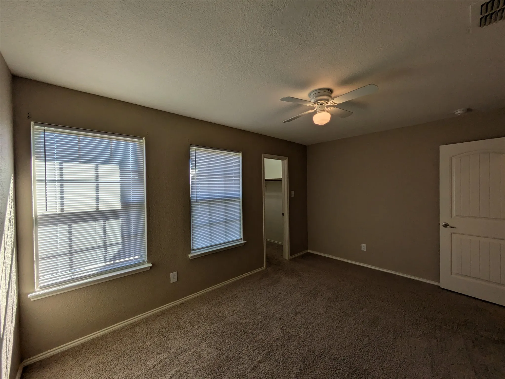 Empty room with a textured ceiling, dark colored carpet, and ceiling fan