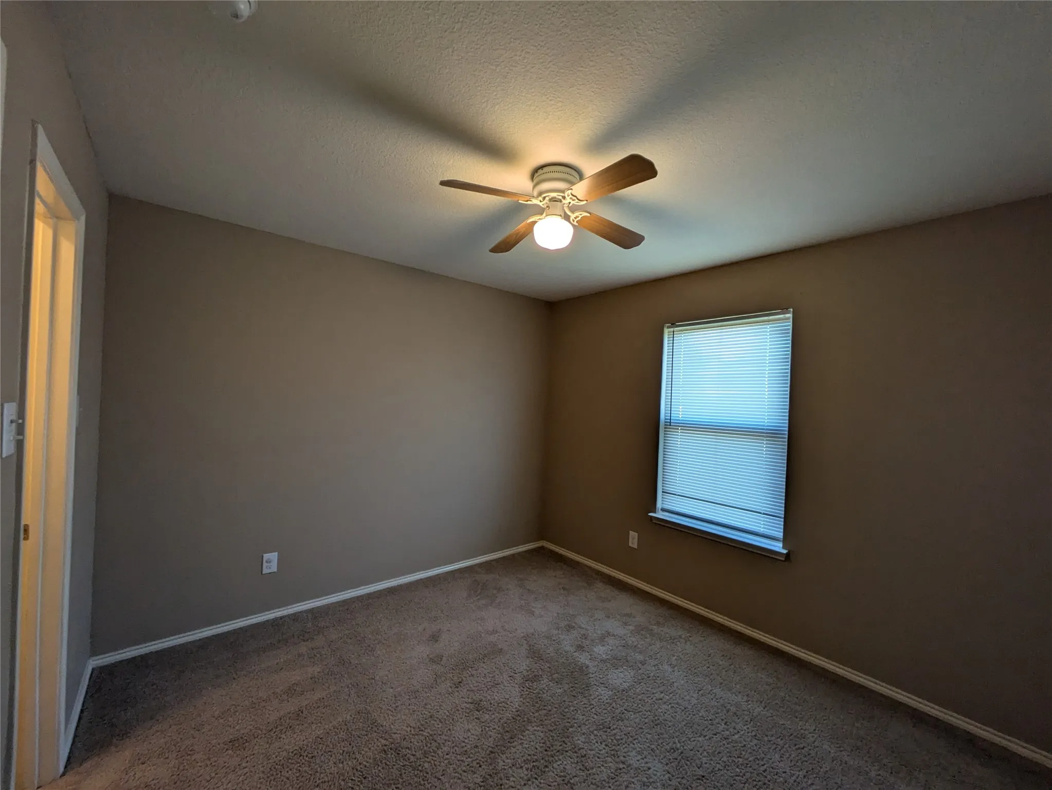 Spare room featuring a textured ceiling, dark carpet, and ceiling fan