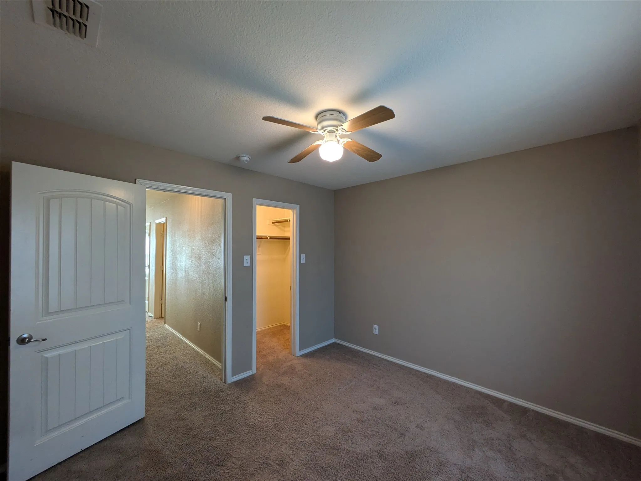 Unfurnished bedroom with a closet, a textured ceiling, ceiling fan, a walk in closet, and carpet