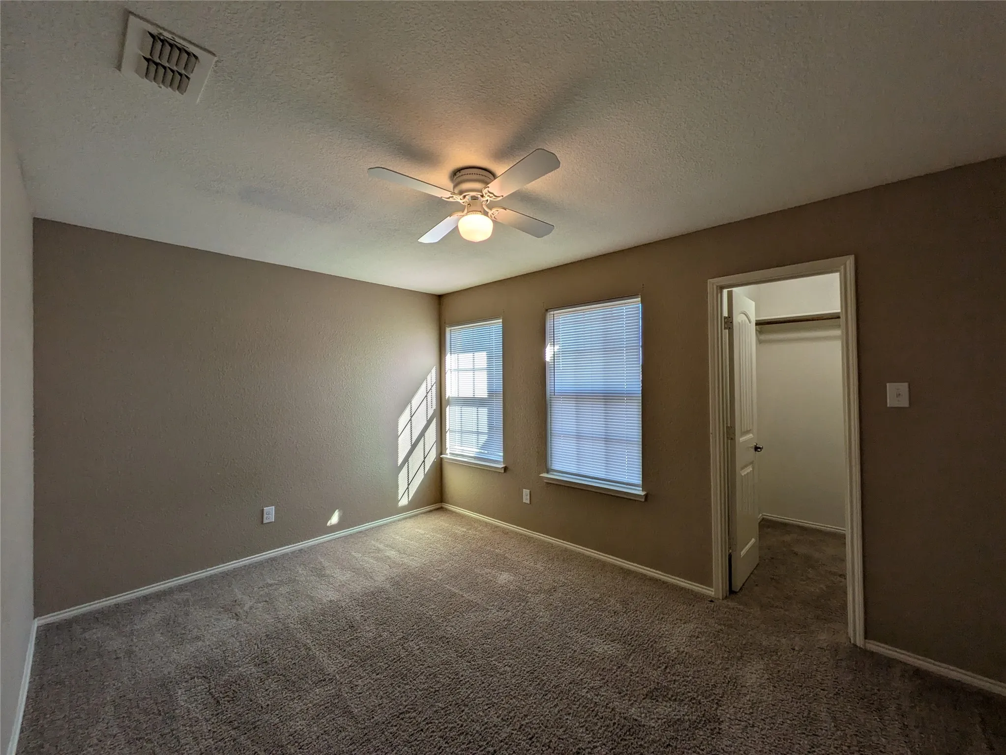 Unfurnished bedroom featuring ceiling fan, dark carpet, a textured ceiling, and a spacious closet